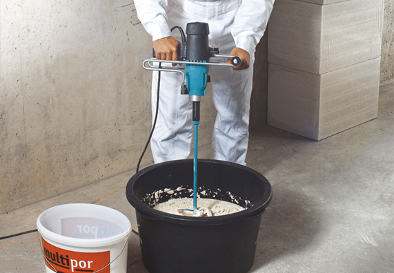 Egy barkácsoló könnyű habarcsot kever be keverőgéppel egy vödörben.