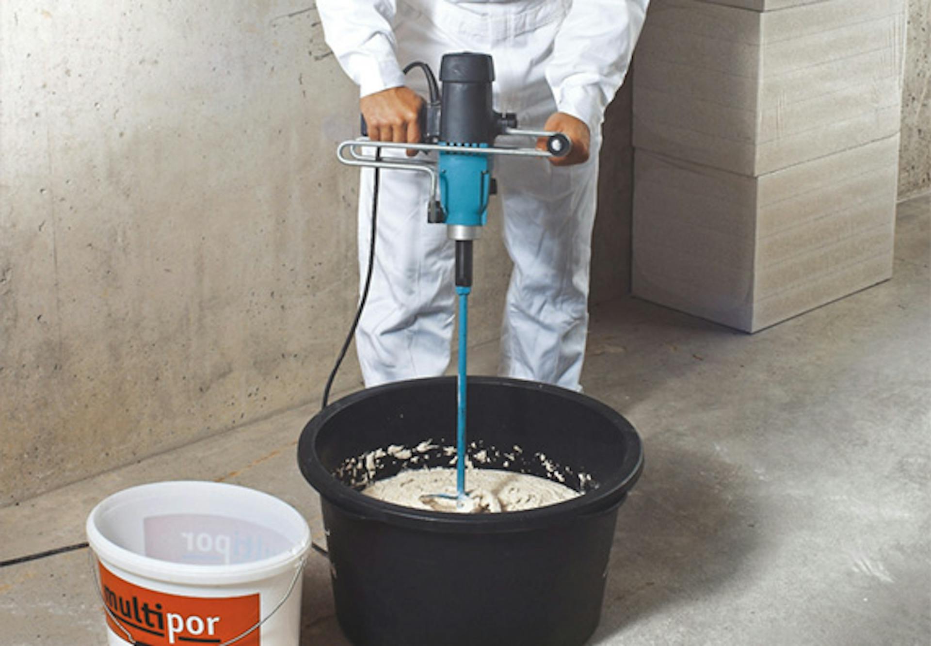 Un appassionato del fai da te miscela la malta leggera con l’agitatore in un secchio.
