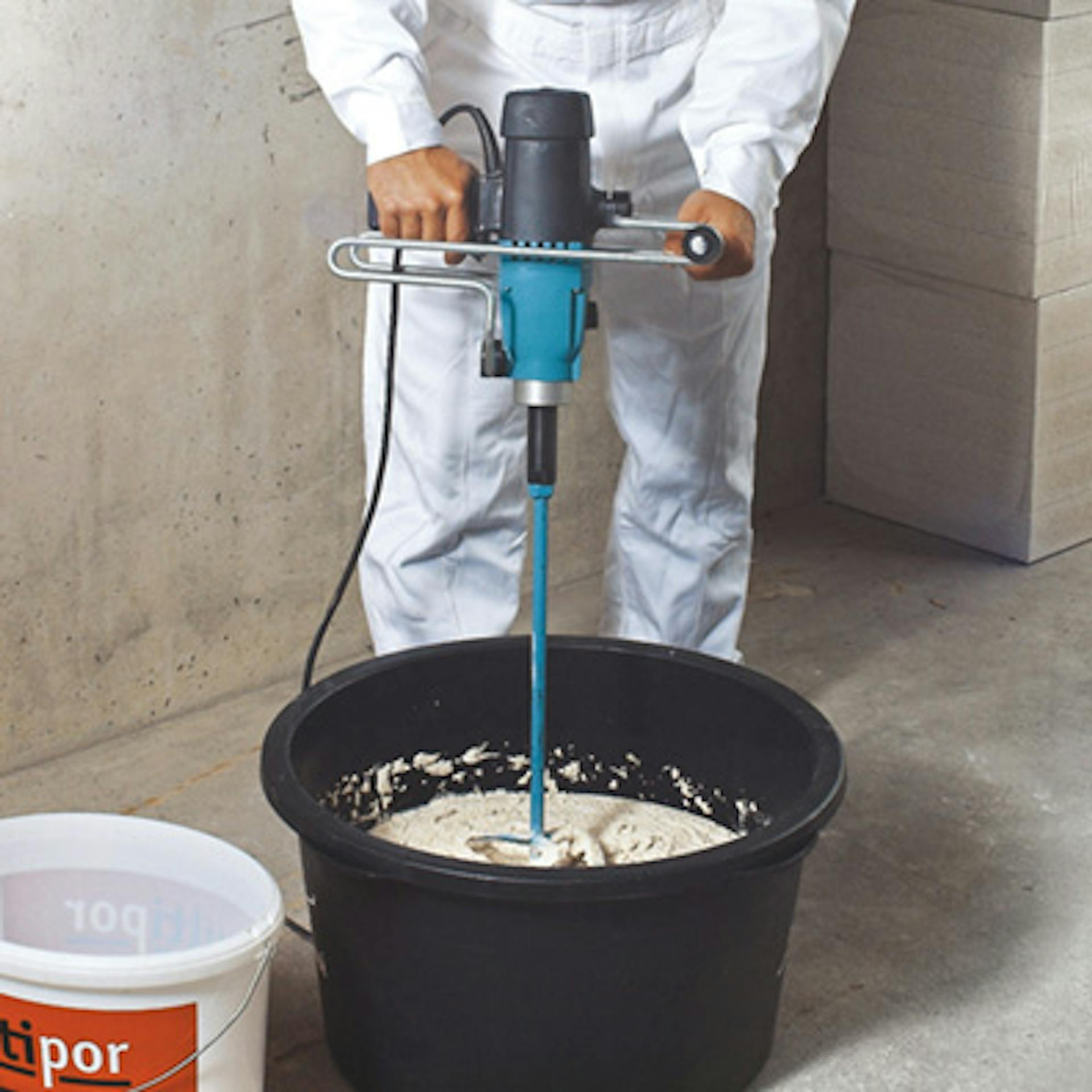 Egy barkácsoló könnyű habarcsot kever be keverőgéppel egy vödörben.