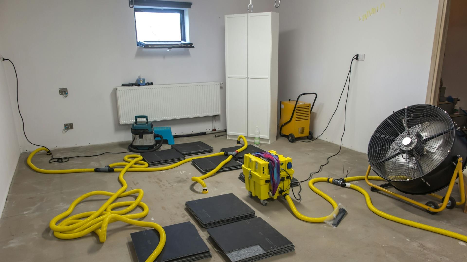 Kellerraum mit großem Trocknungsventilator, und Geräten, die die Feuchtigkeit aus dem Boden ziehen.