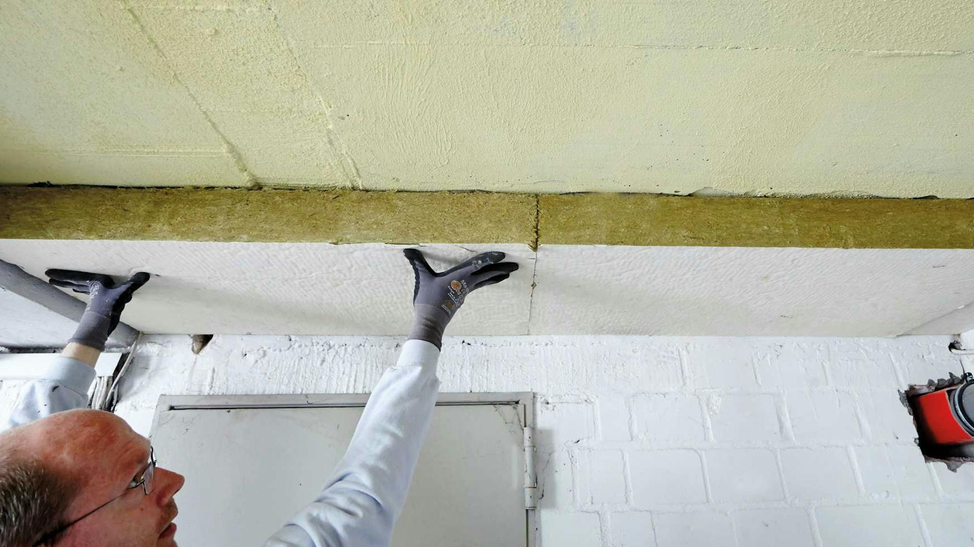 Mann befestigt Dämmmaterial An Kellerdecke.