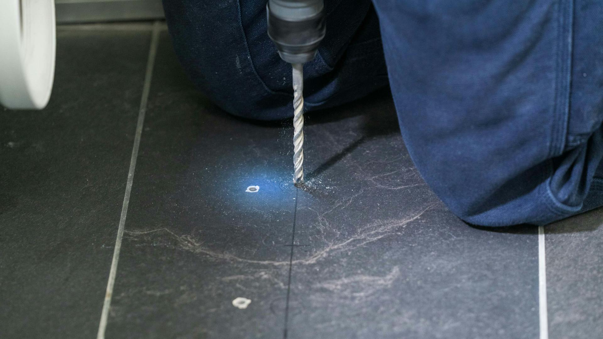 Jemand bohrt ein Loch in dunkle Fliesen.