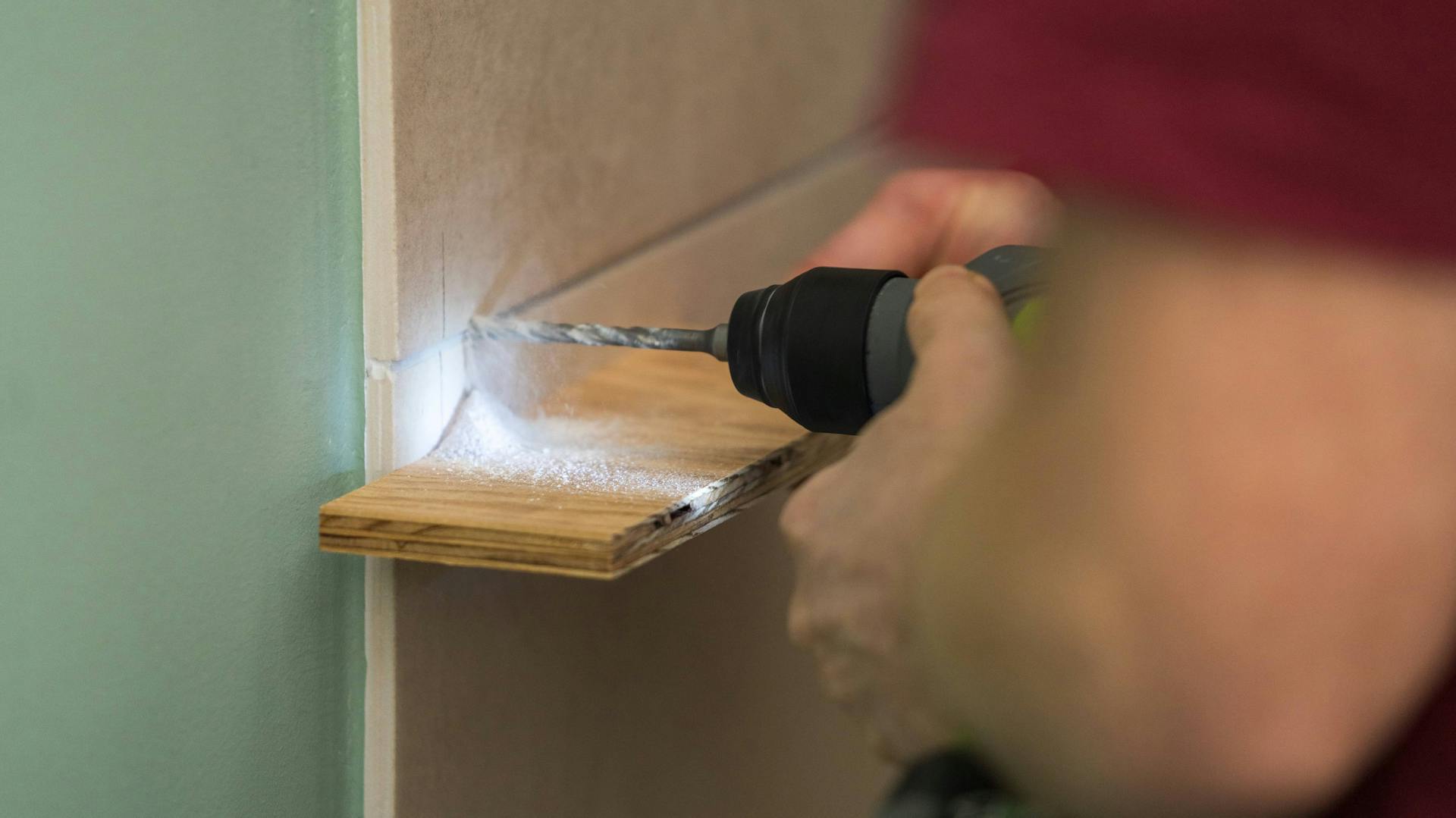 Jemand bohrt ein Loch in eine Fliesenfuge.