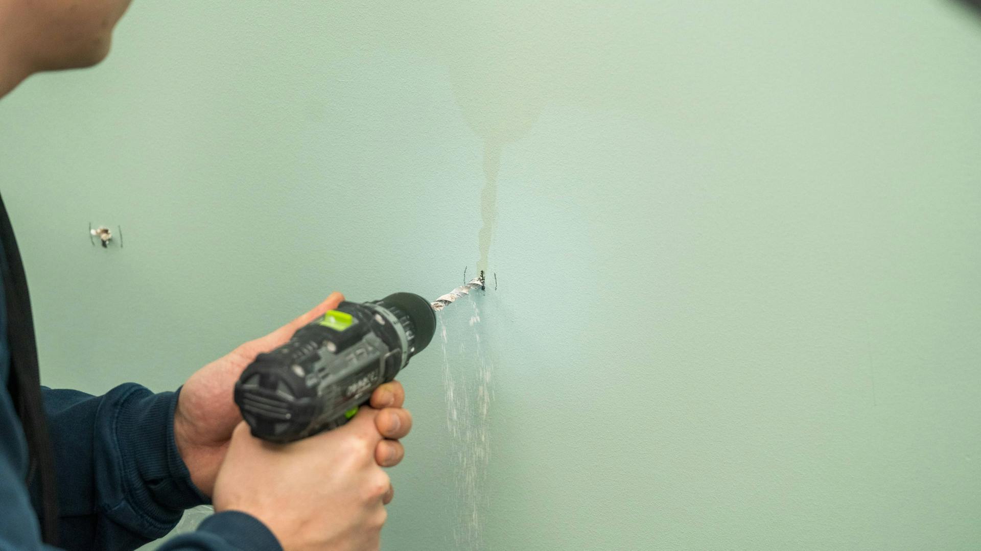 Jemand bohrt ein Loch in eine Gipskartonwand.
