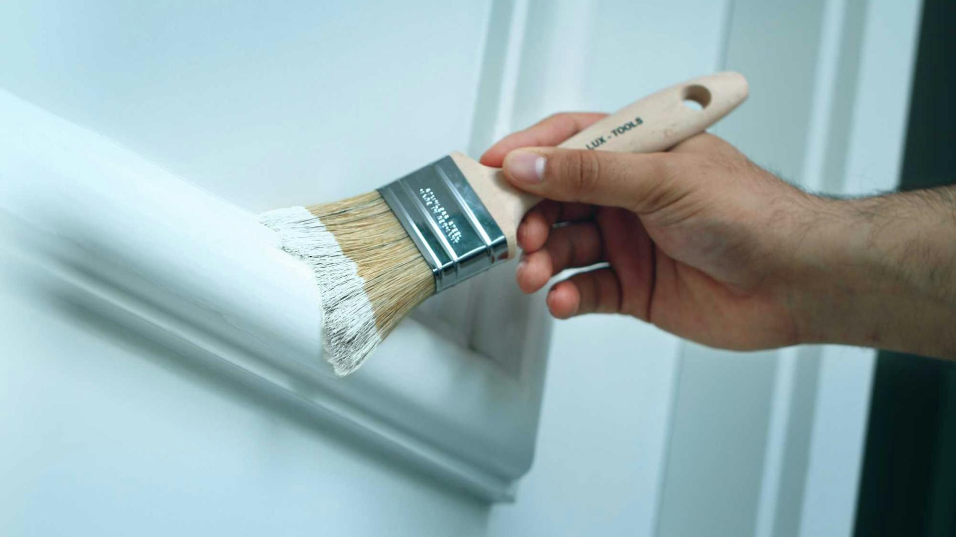 Heimwerker streicht Tür mit Pinsel in weißer Farbe.