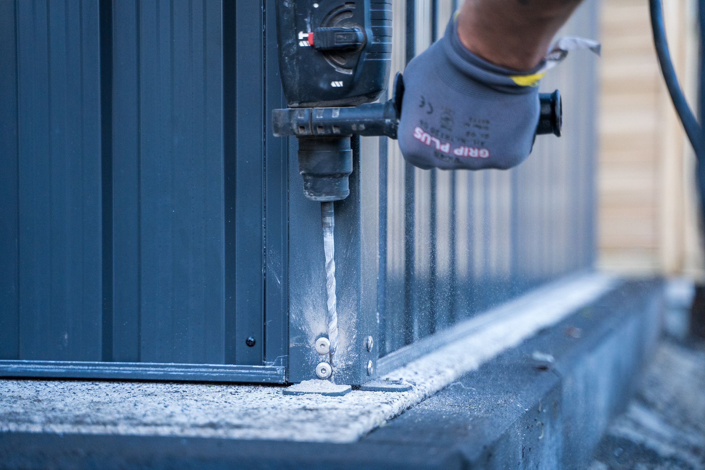 Egy ember furatokat készít egy járólap alapba egy szerszámosház rögzítéséhez.