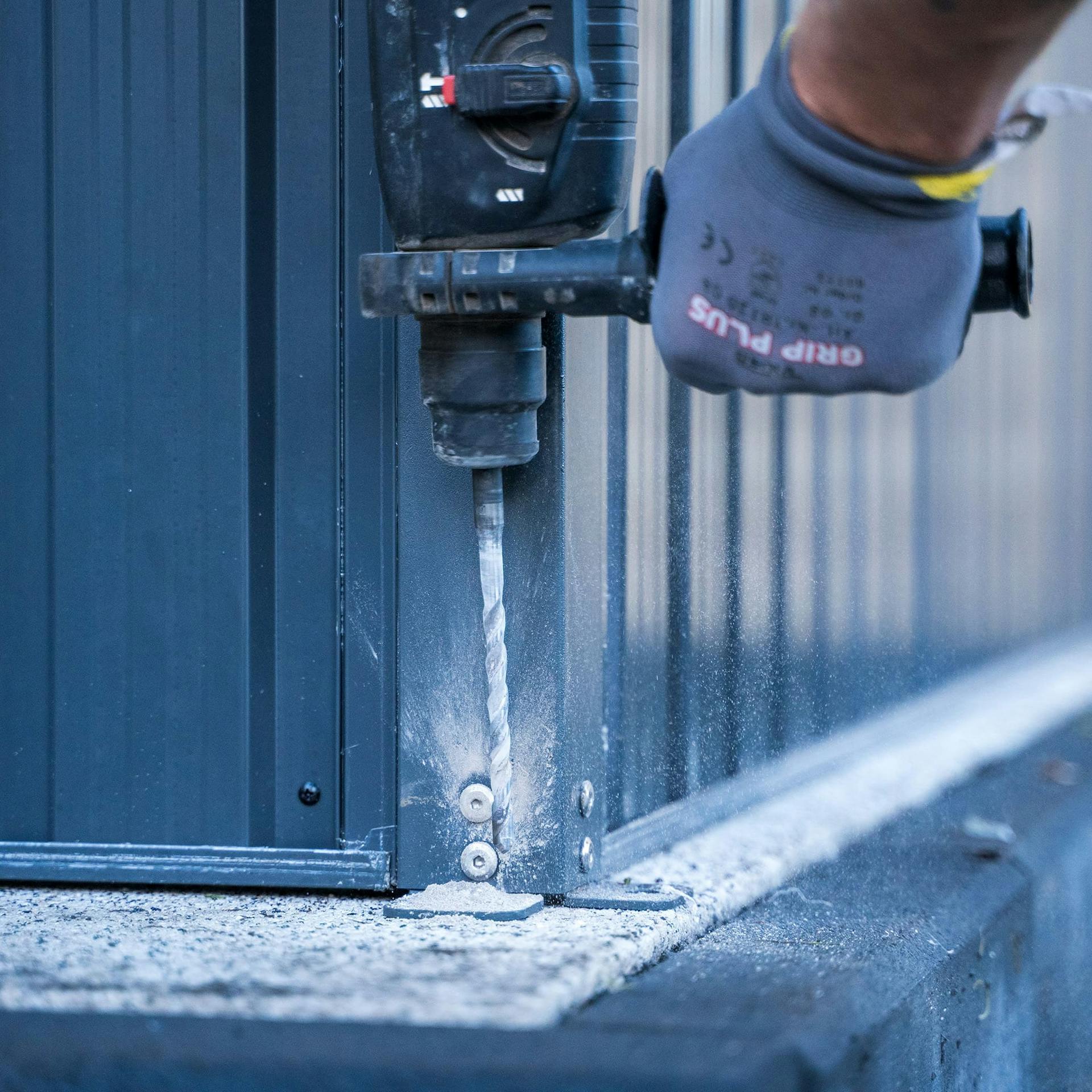 Egy ember furatokat készít egy járólap alapba egy szerszámosház rögzítéséhez.