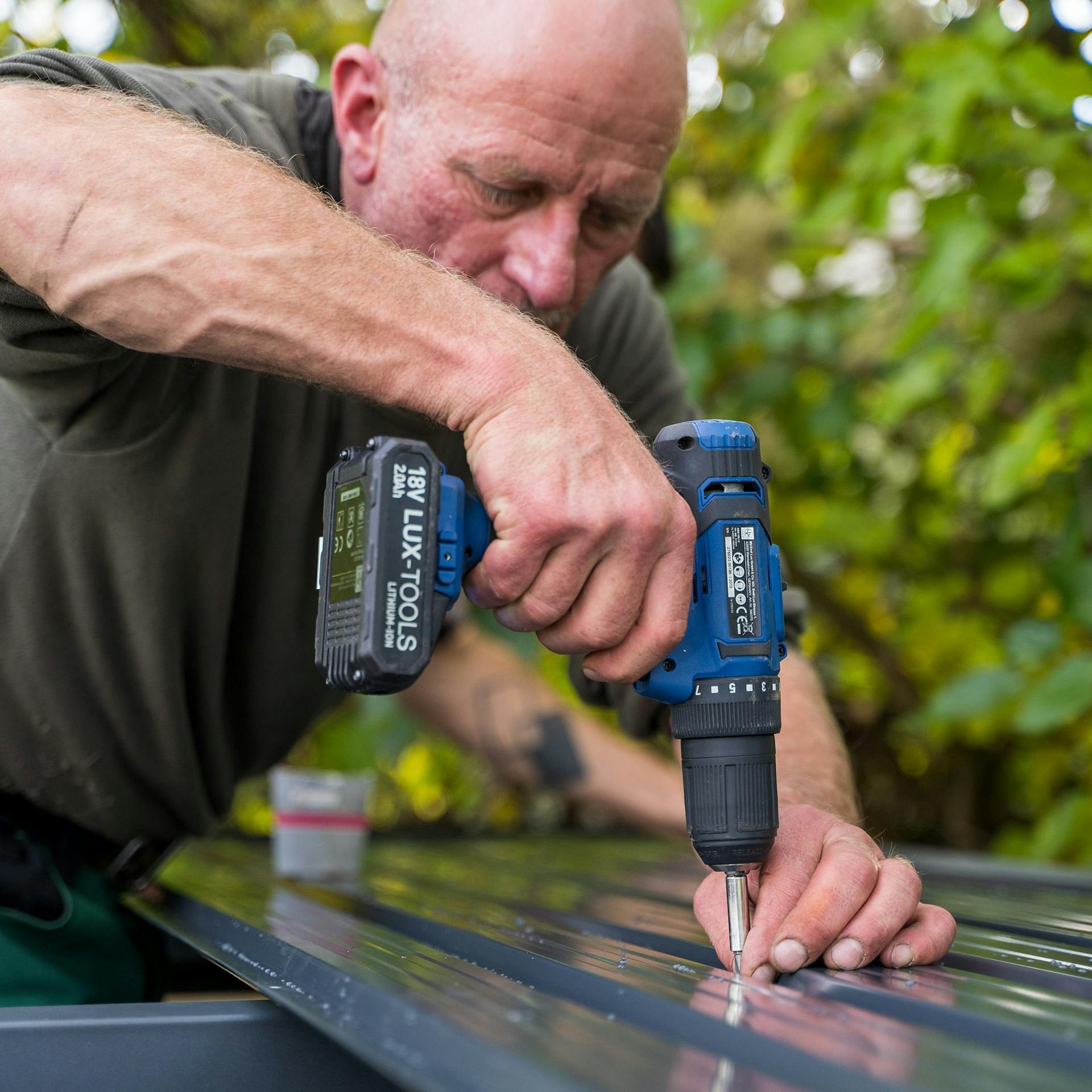 Egy férfi egy fém szerszámosház tetejét csavarozza fel.