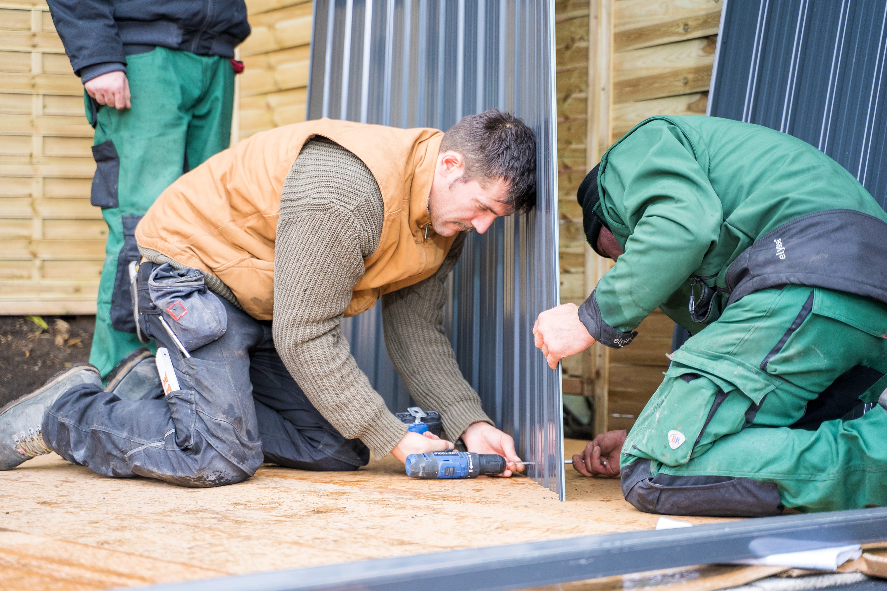 Három ember szereli egy fém szerszámosház oldalfalait