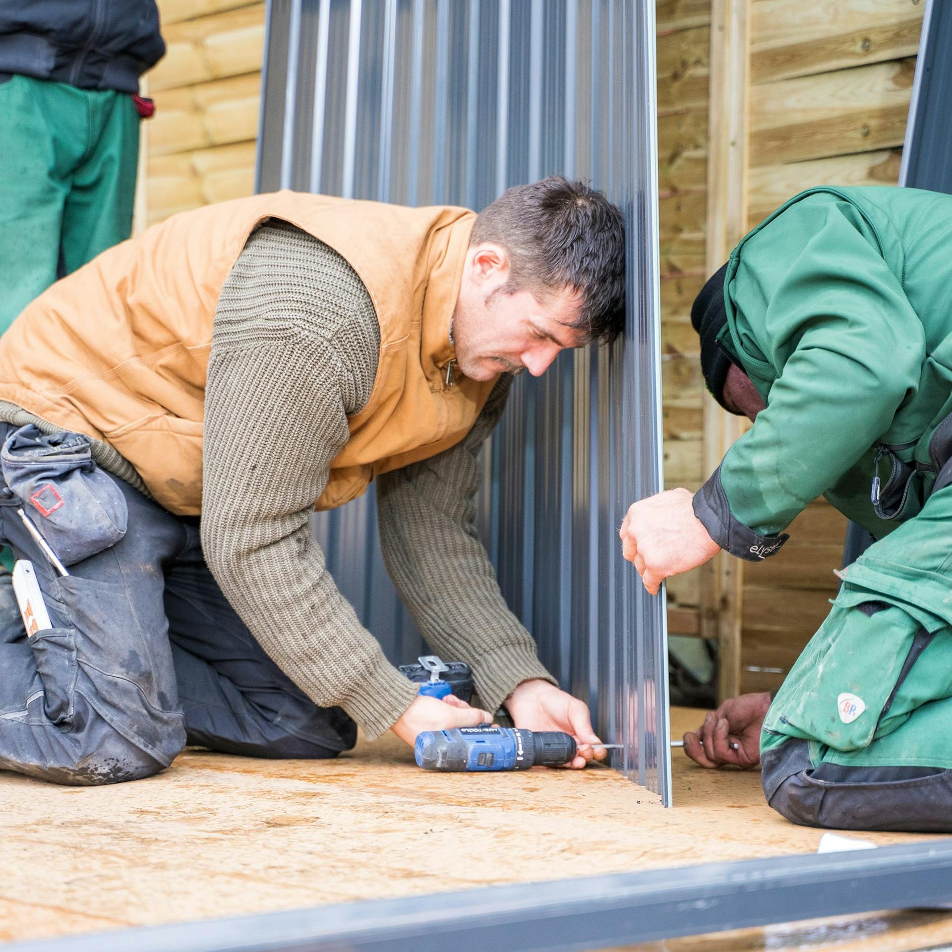 Három ember szereli egy fém szerszámosház oldalfalait