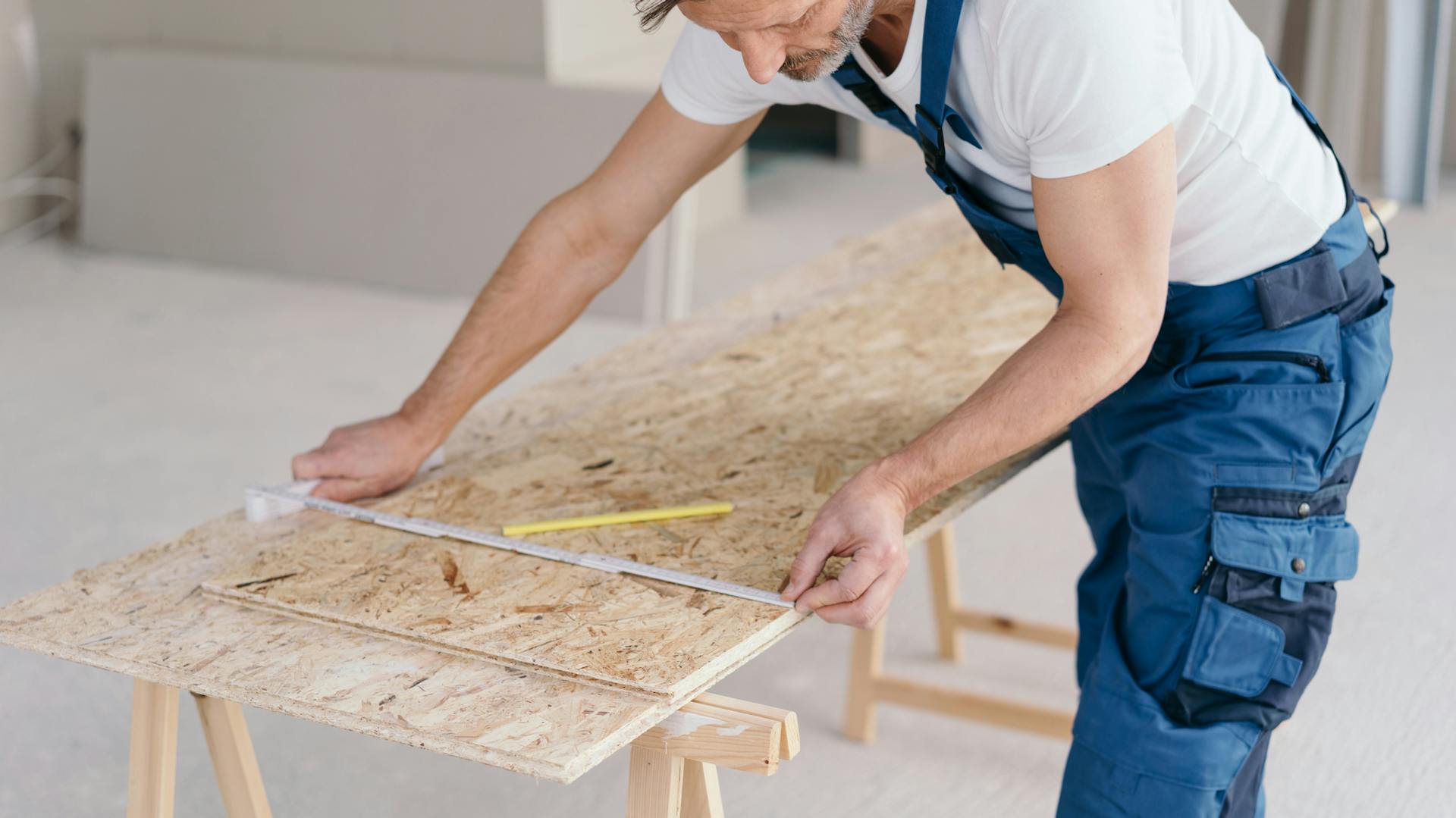 Muž vymeriava OSB dosku na stole na tapetovanie