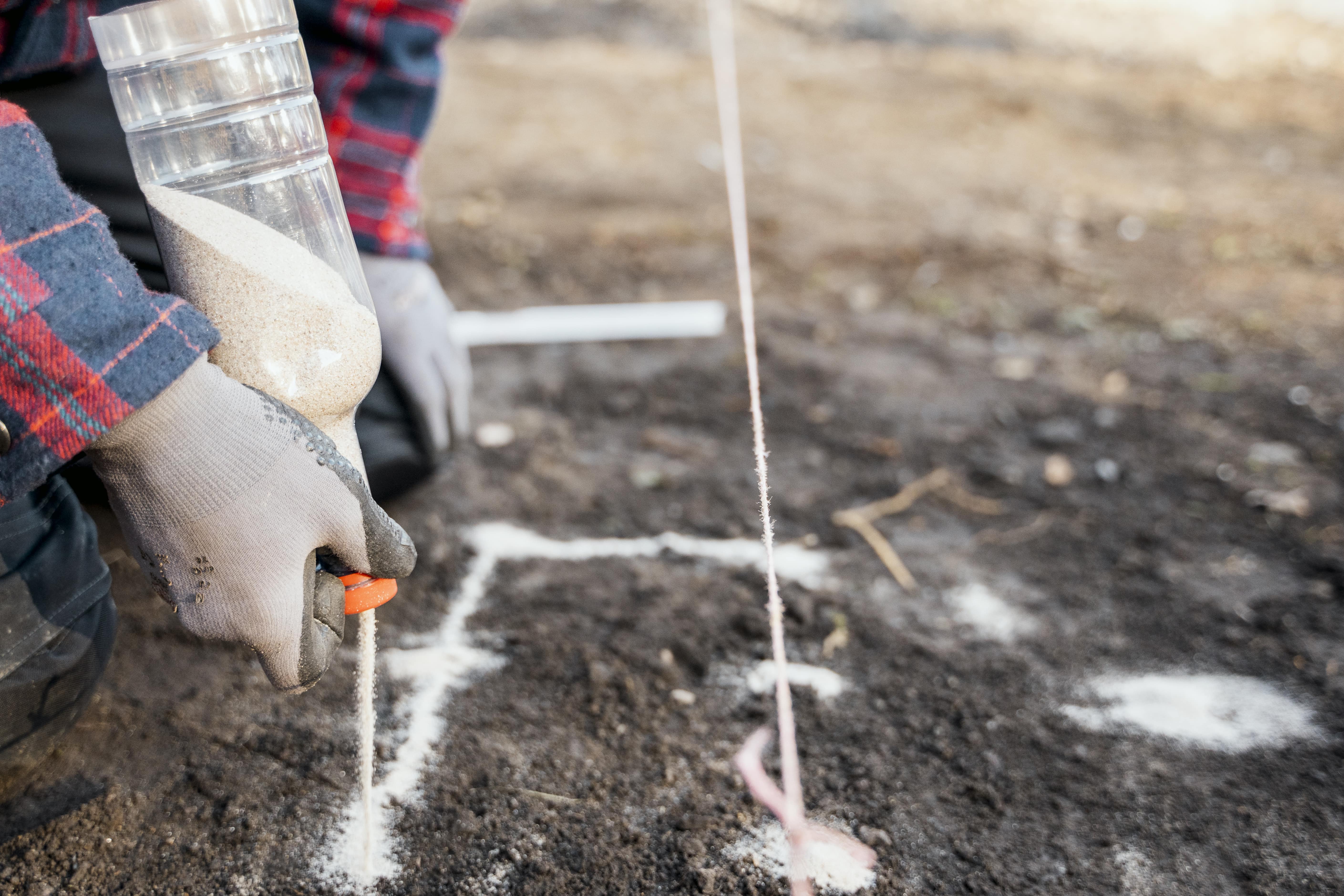 Heimwerker markiert die Stellen für das Punktfundament mit Sand.