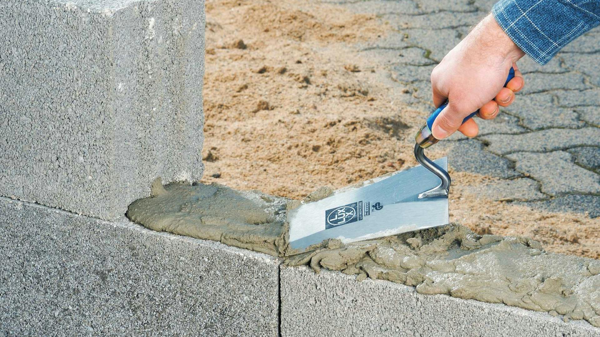 Heimwerker gibt mit der Maurerkelle Mörtel auf eine Mauer