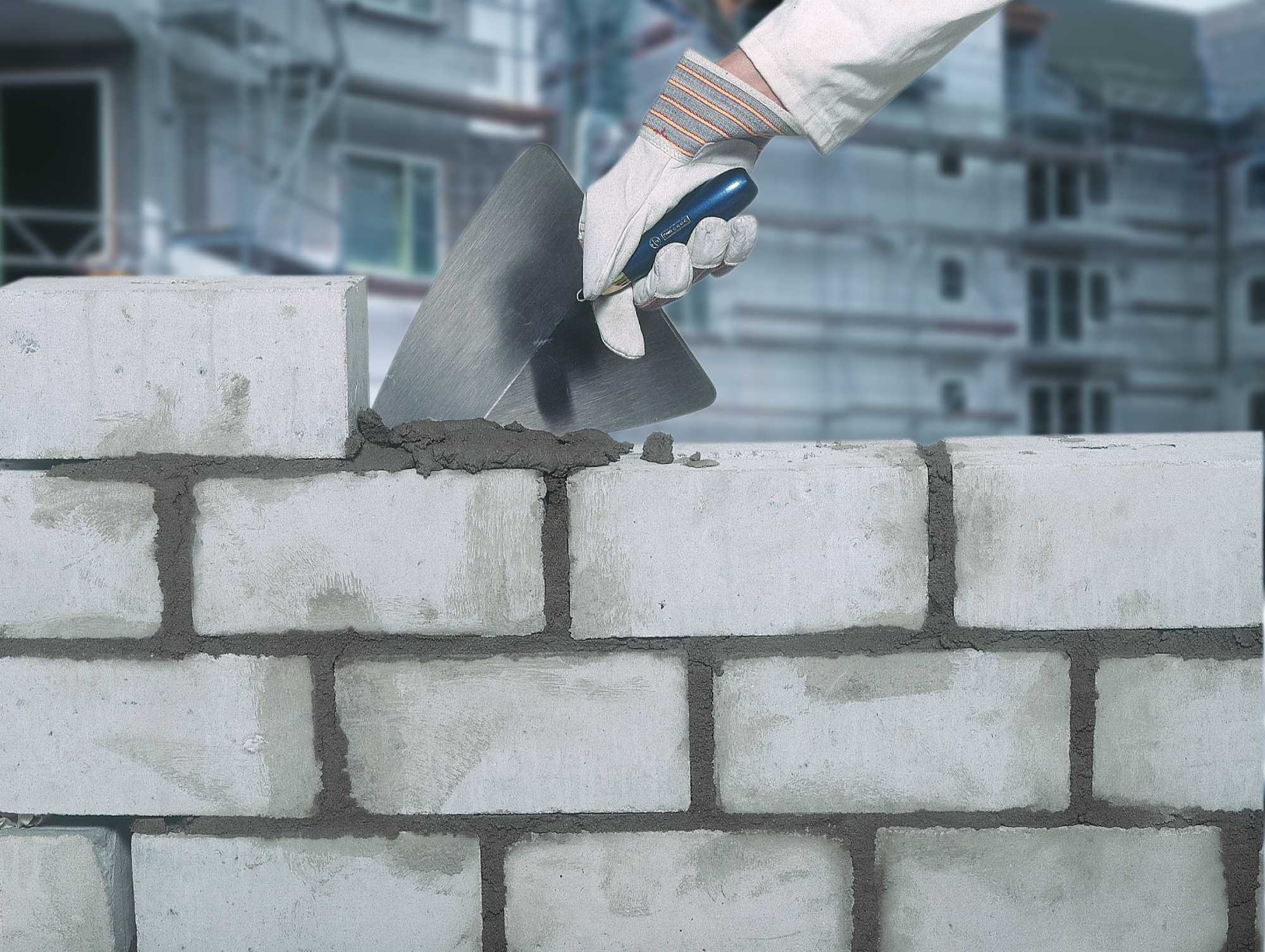 Eine Mauer wird mit Kelle und Zement gebaut.