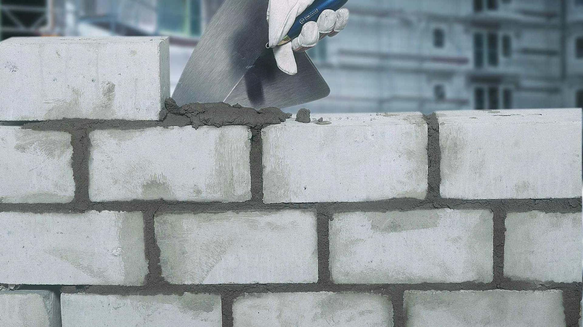 Eine Mauer wird mit Kelle und Zement gebaut.