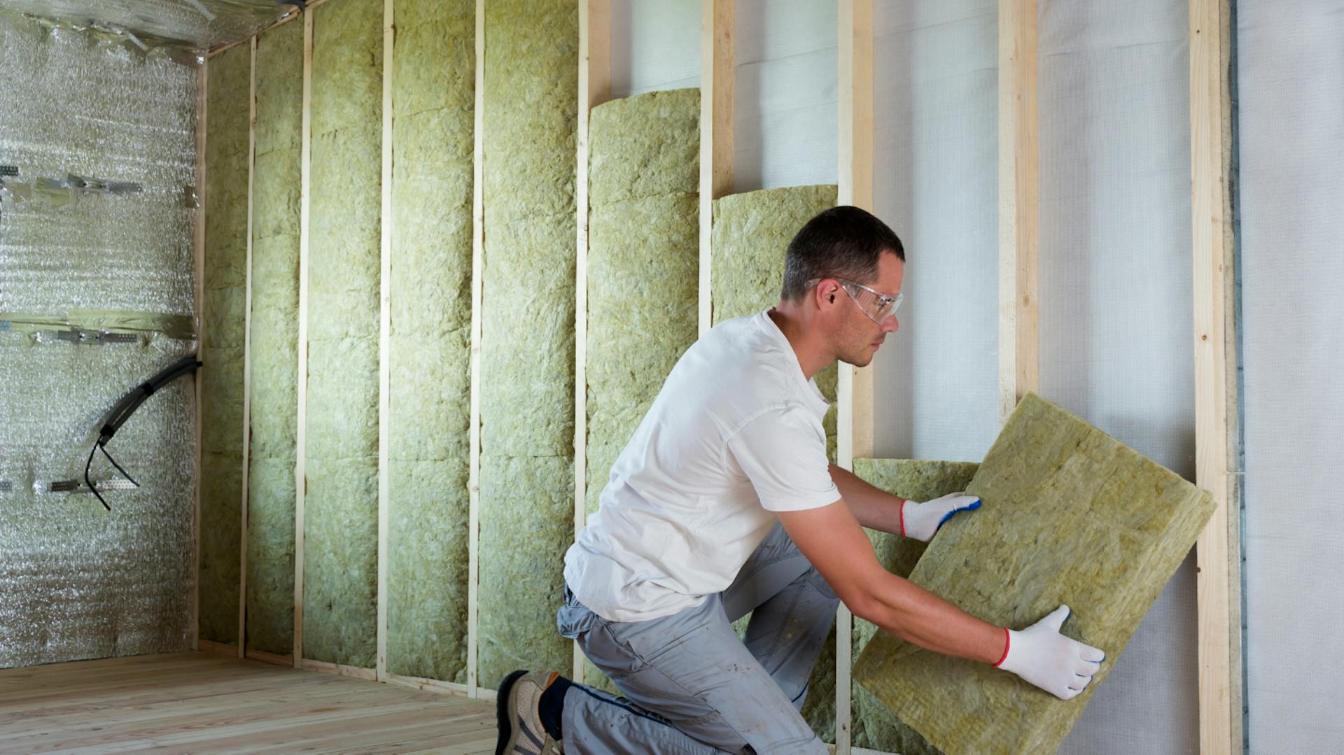Person dämmt Wand mit Dämmmaterial.