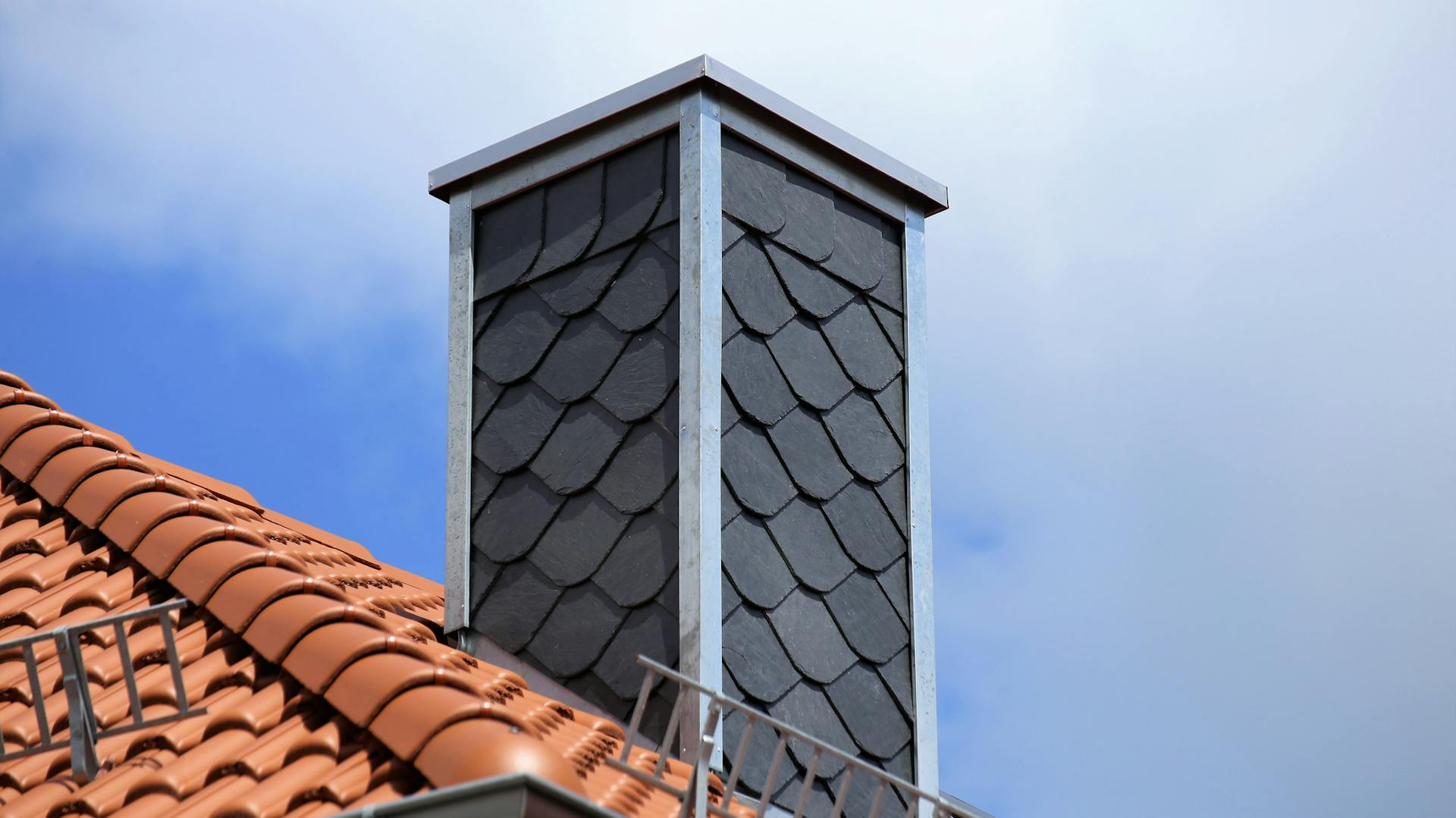 Grau verkleideter Schornstein auf einem Ziegeldach