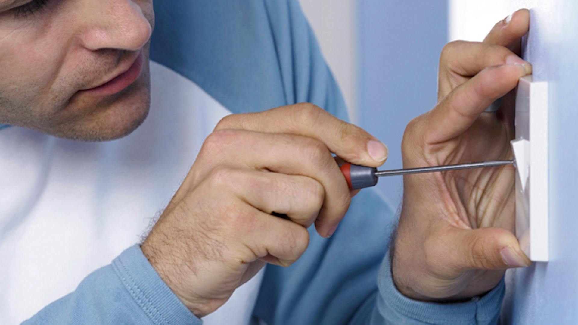 Férfi csavarhúzóval a villanykapcsolónál