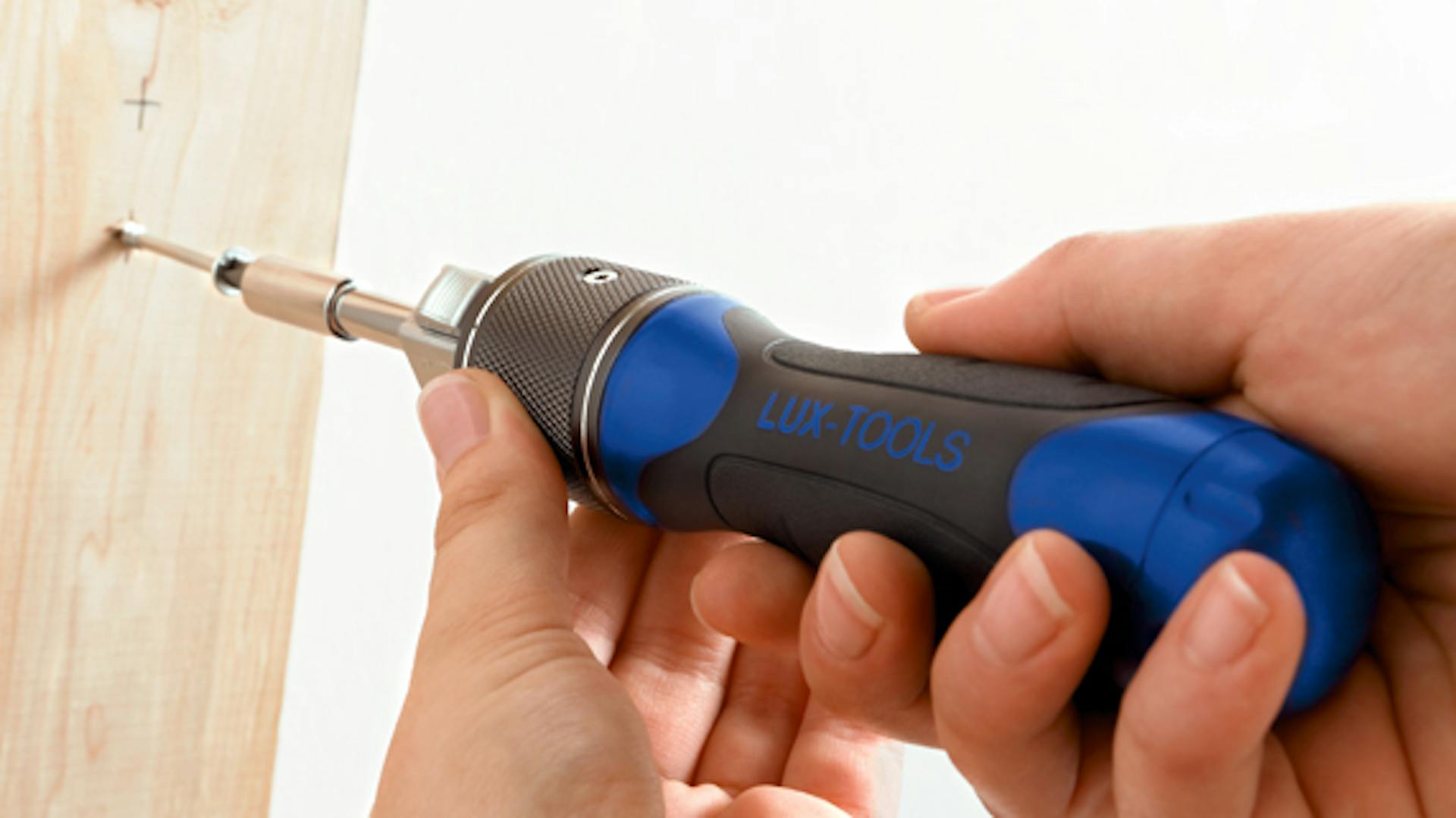 A kezek egy csavarhúzót és egy csavart tartanak a faanyaghoz