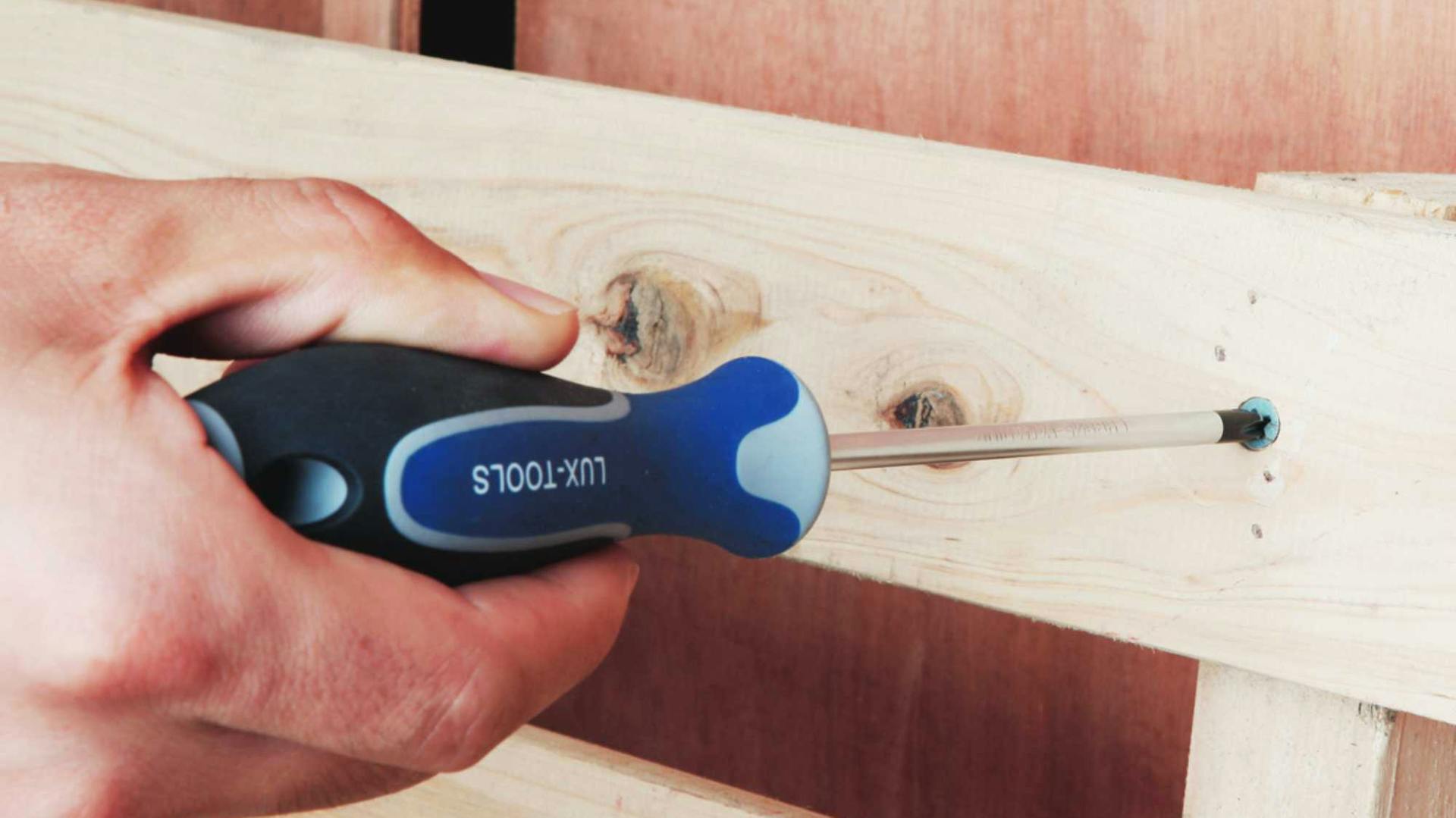 Hand dreht Schraube in Holzbank mit Schraubendreher