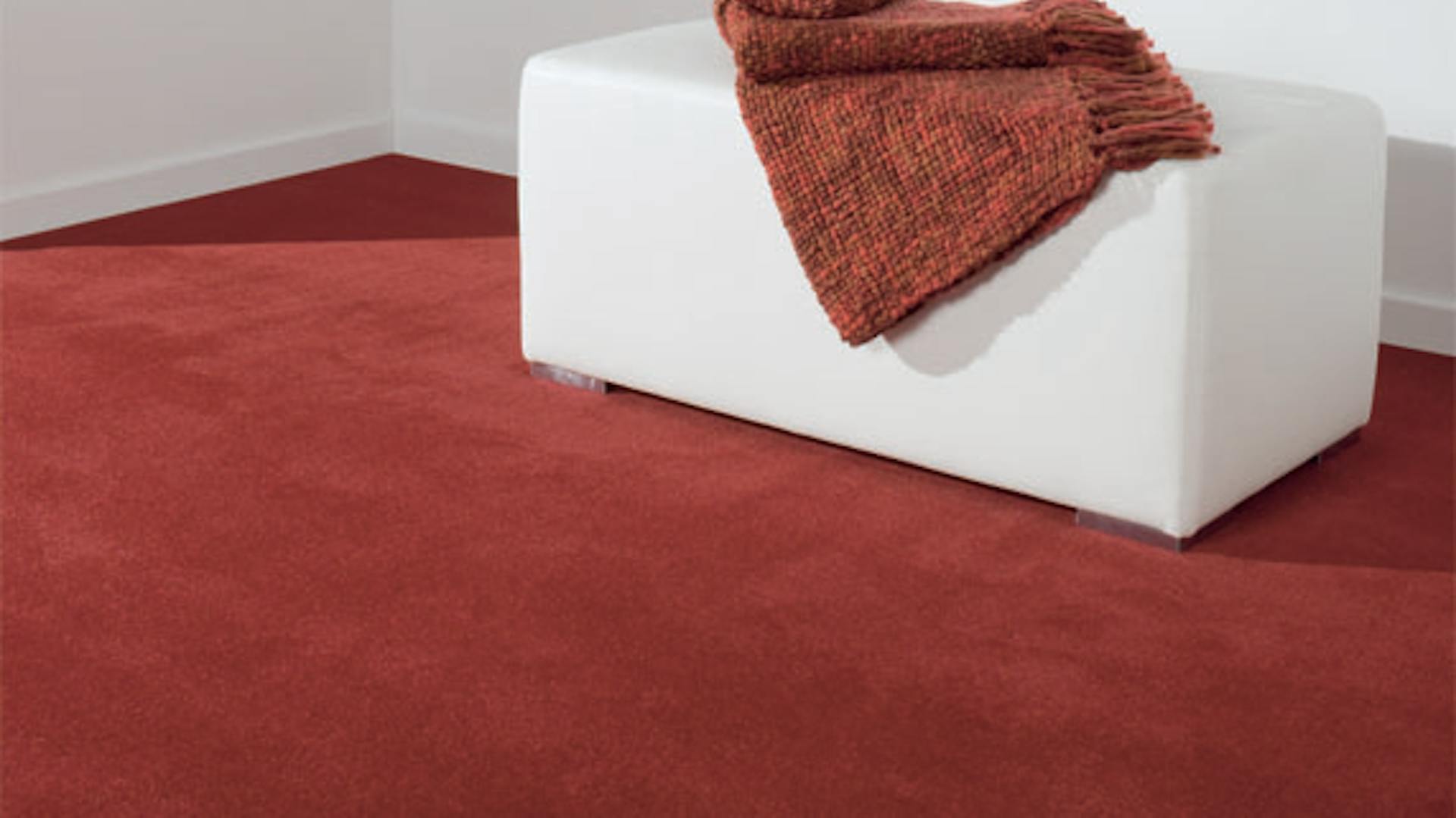Roter Veloursteppichboden mit einem weißen Sofahocker.