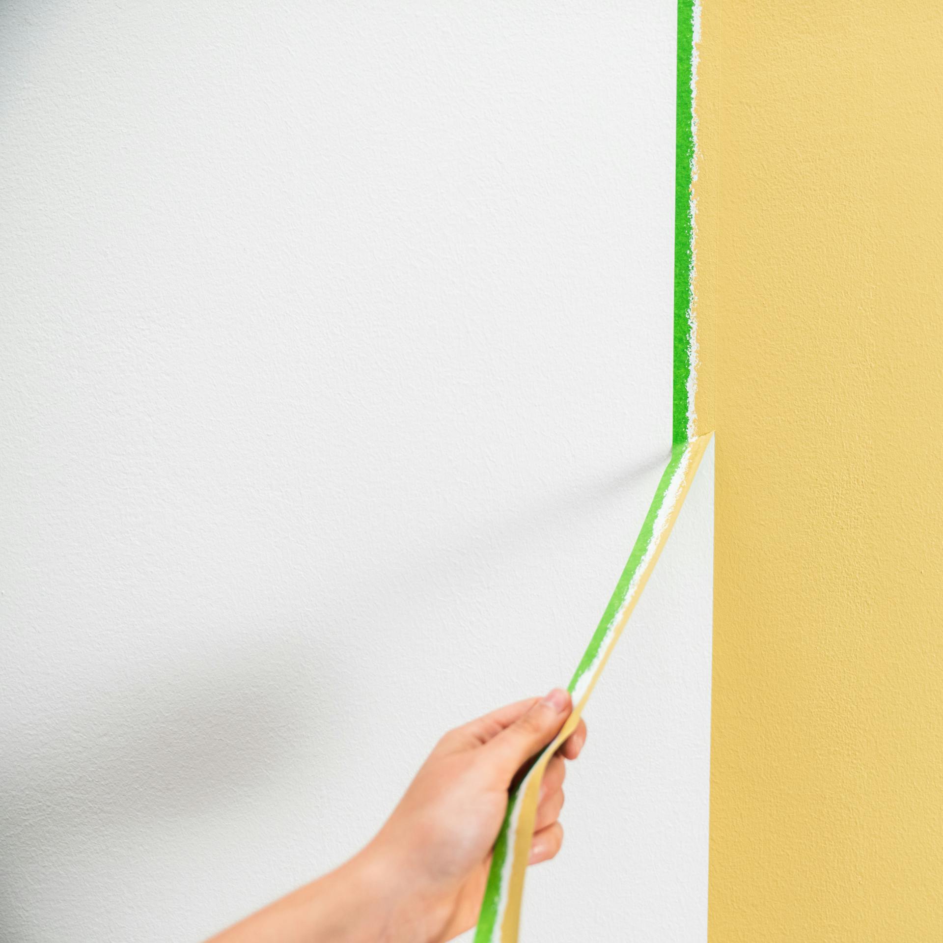 Person zieht Malerkrepp von der Wand ab.