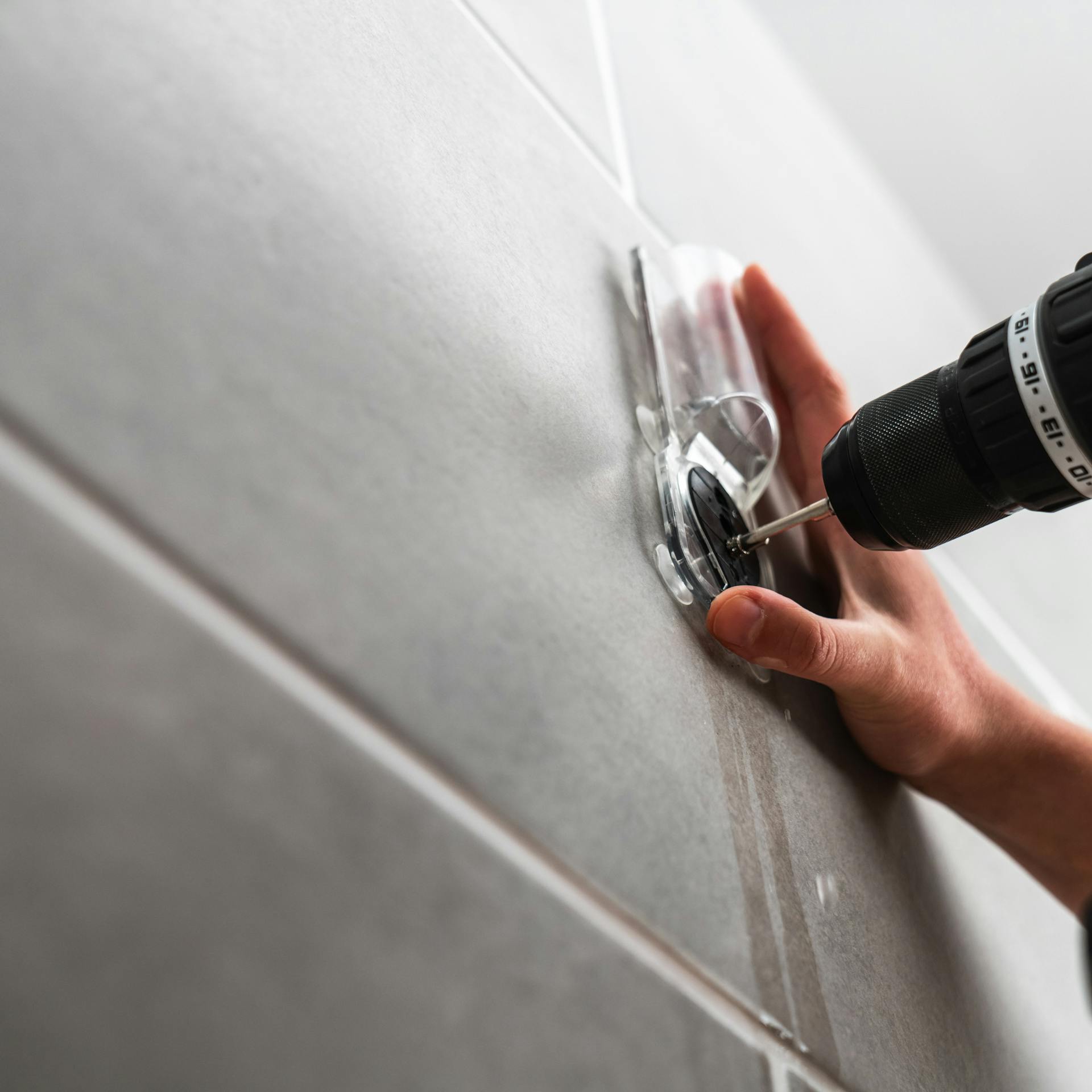 Person schraubt in eine Fliese mithilfe einer Führung.