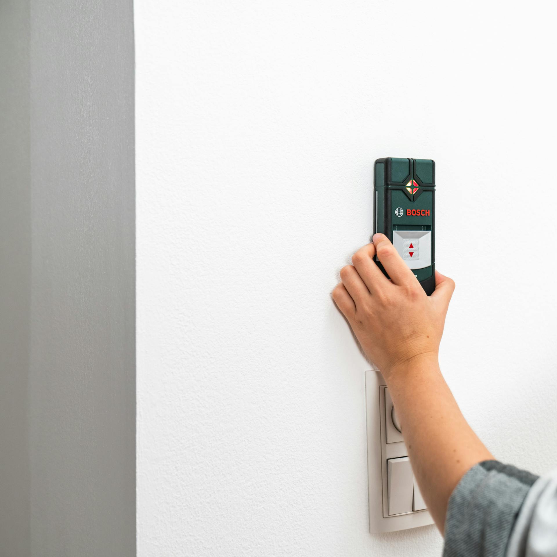 Person hält einen Leistungssucher an die Wand.