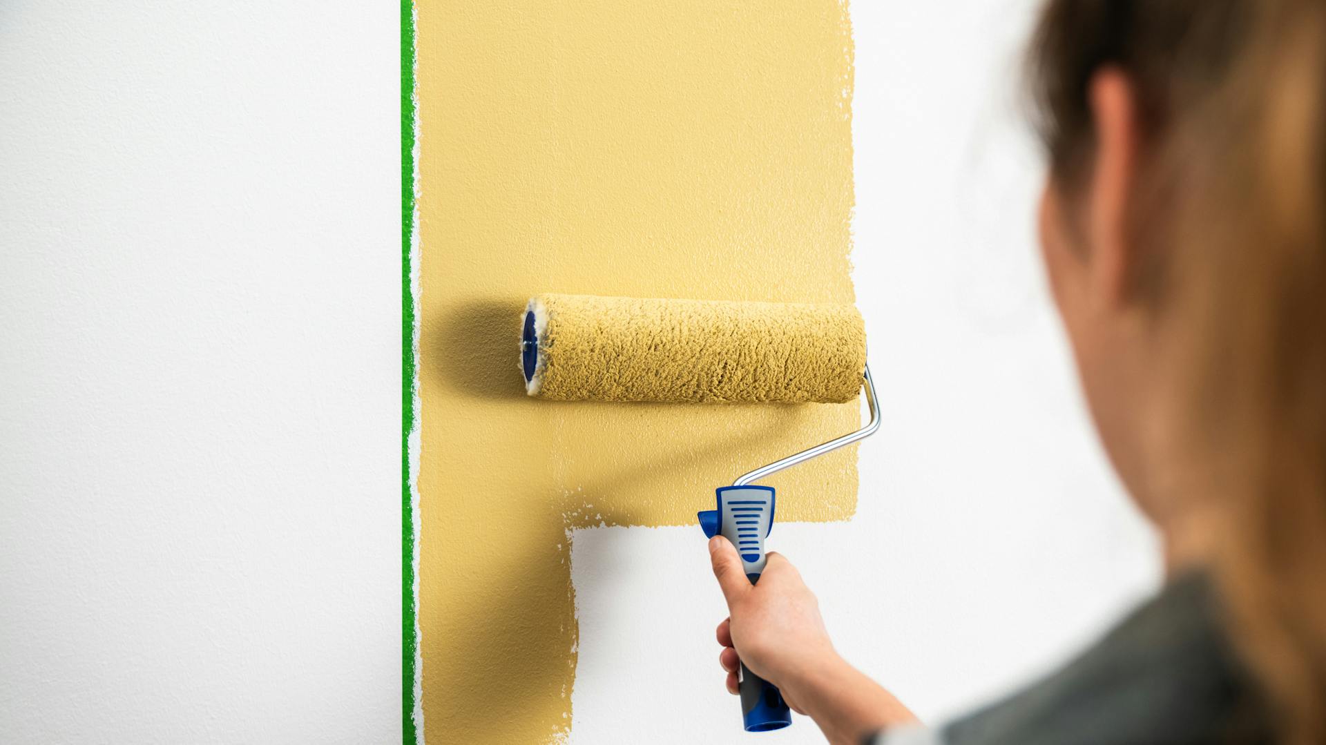 Handwerkerin streicht eine Wand mit einer Farbrolle.