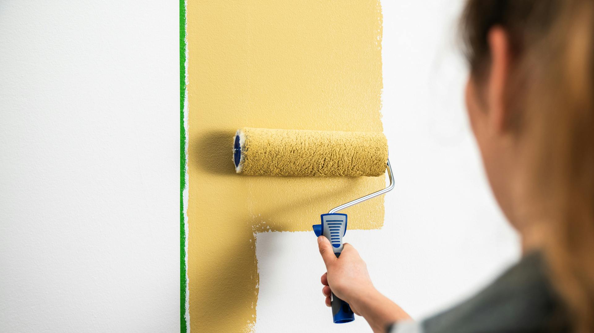 Handwerkerin streicht eine Wand mit einer Farbrolle.