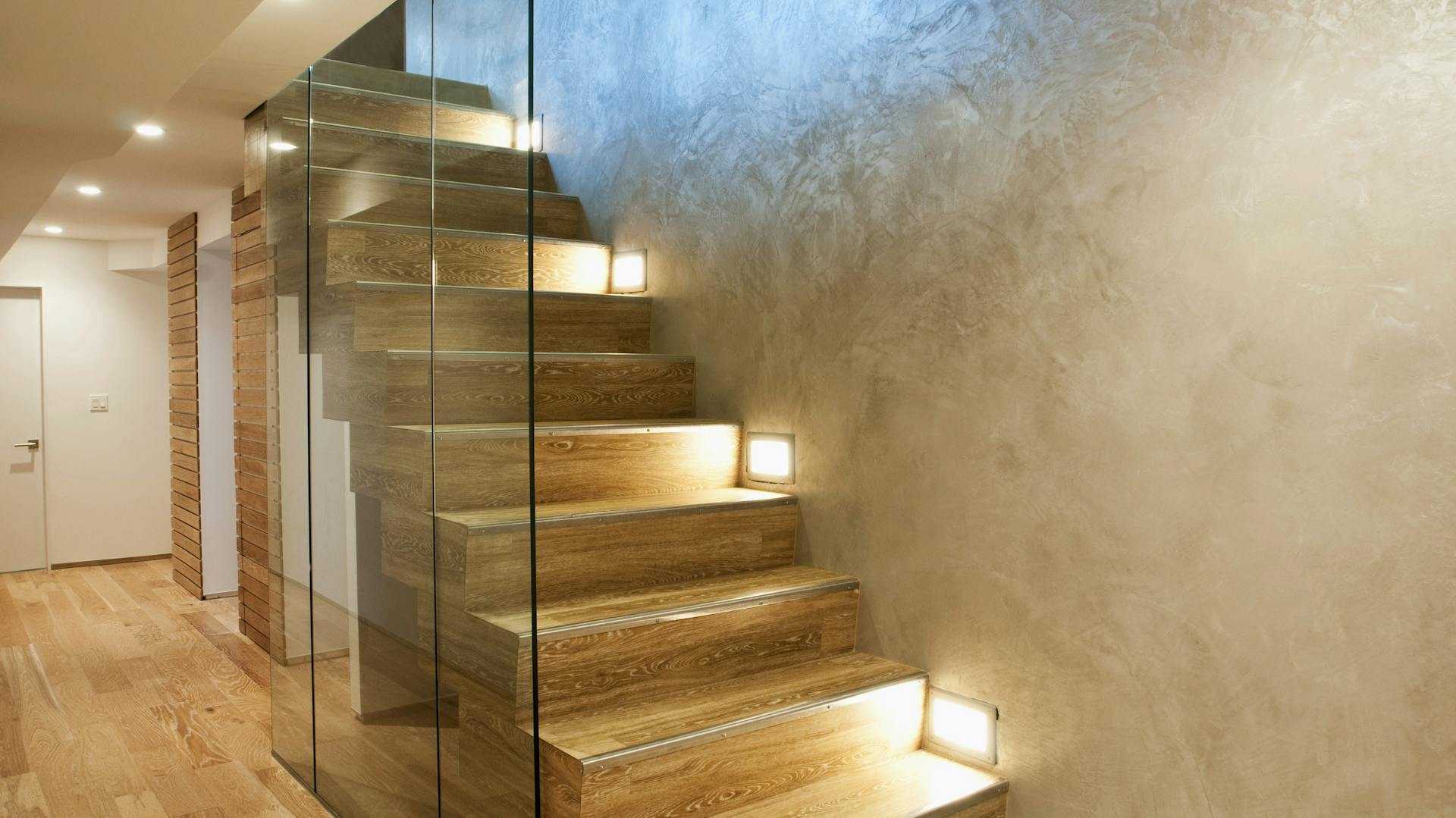 Beleuchtete Holztreppe mit Glaswand und Wandeinbaustrahlern