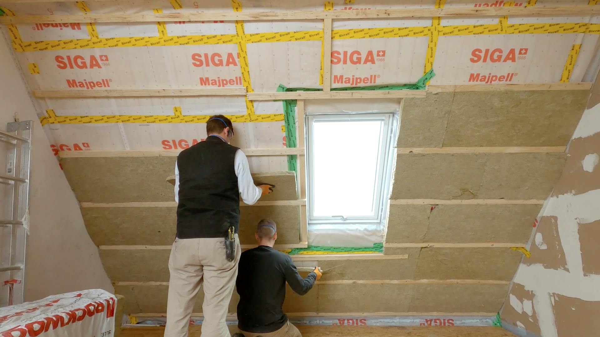 Zwei Personen bringen die Dämmplatten für eine Untersparrendämmung an der Dachschräge an.