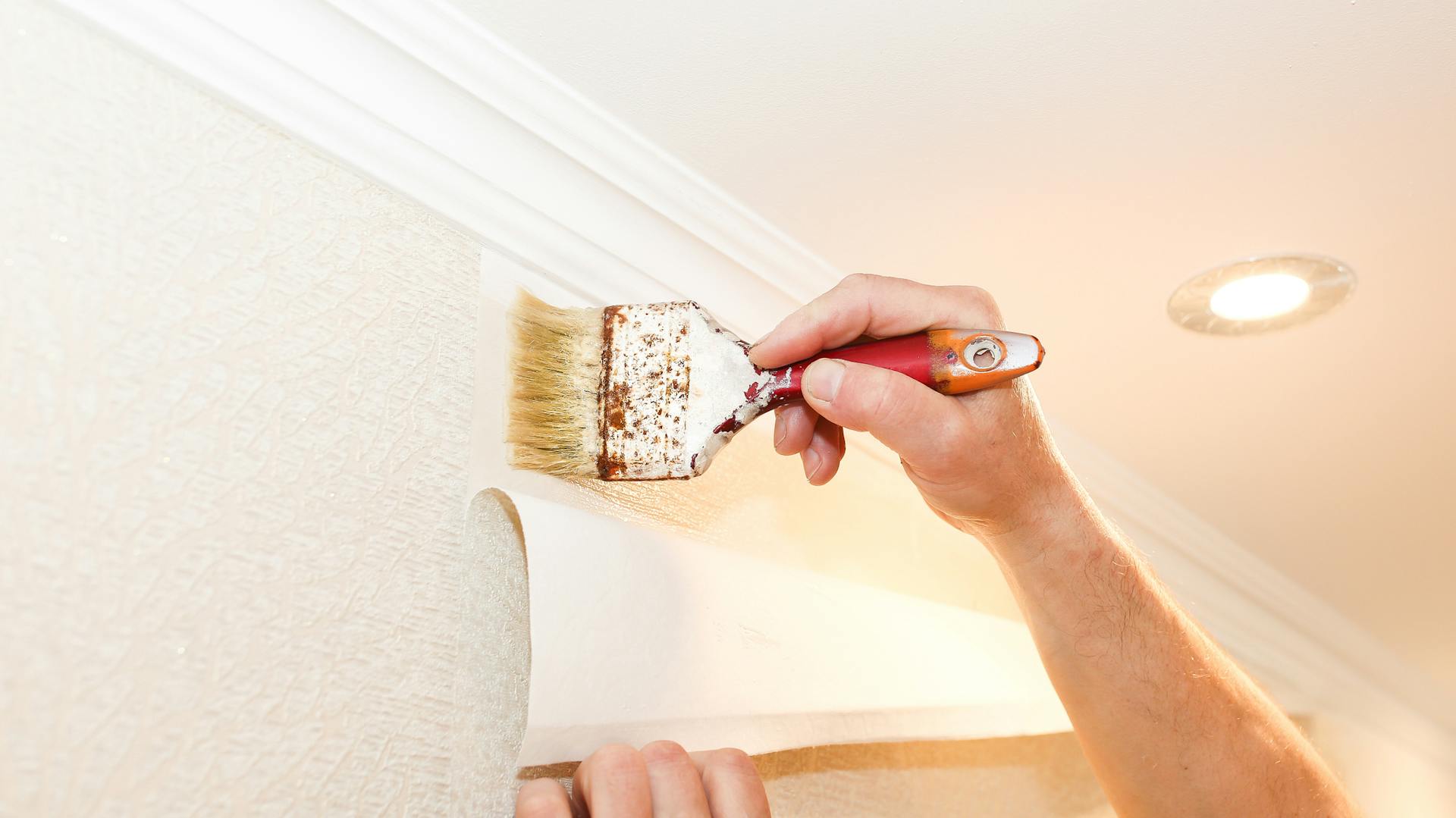 Valaki vlies tapétát ragaszt a falra.