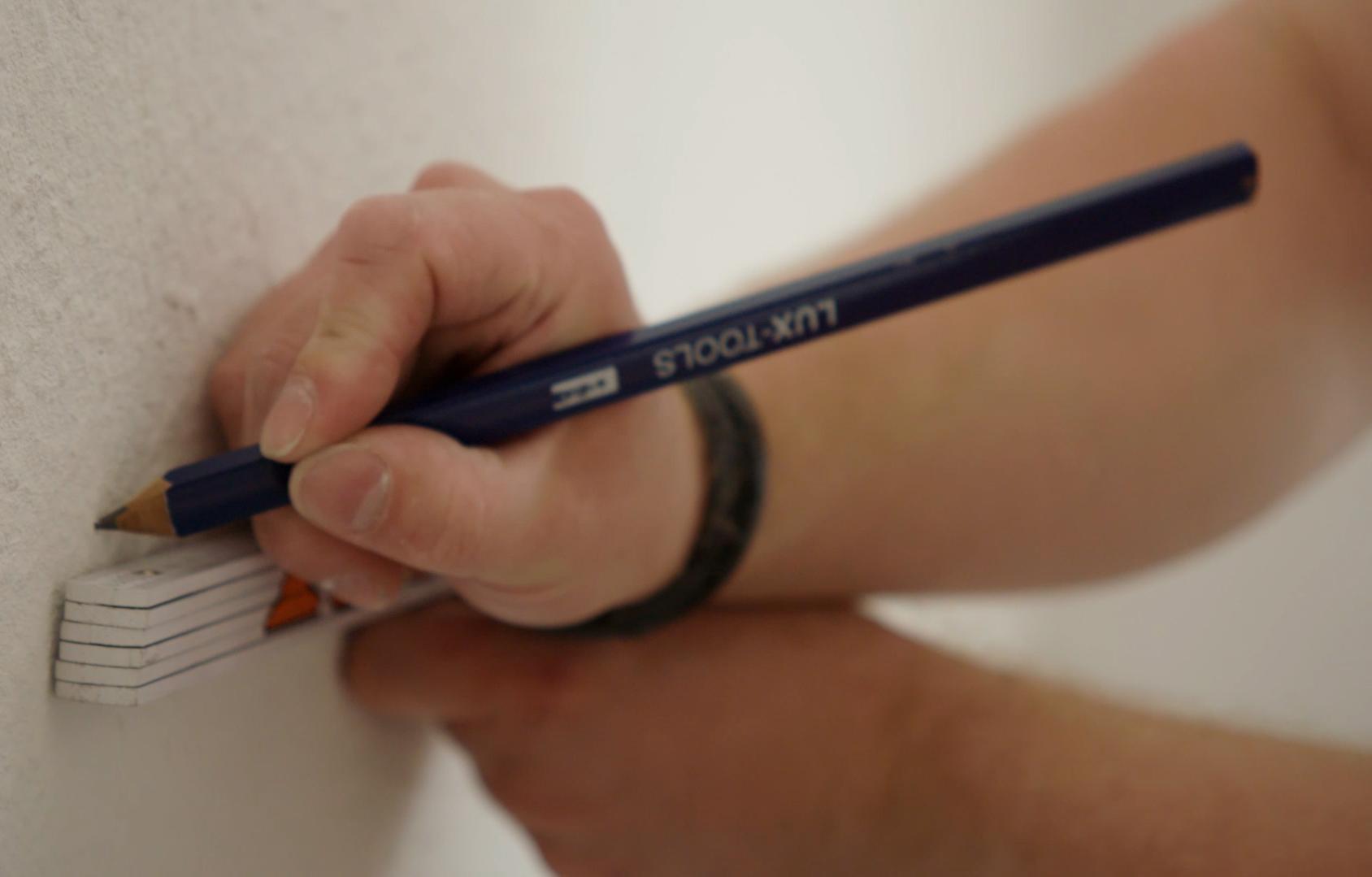 Egy ember felrajzolja a vlies tapéta helyét.