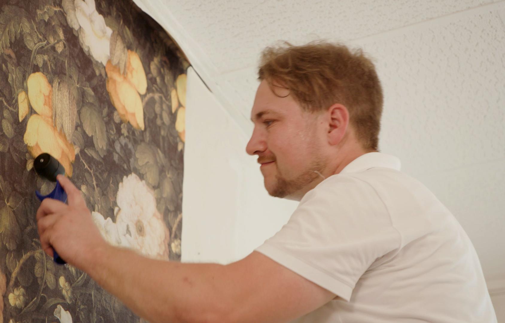 Egy ember eldolgozza a vlies tapéta átmeneteit egy tapétahengerrel.