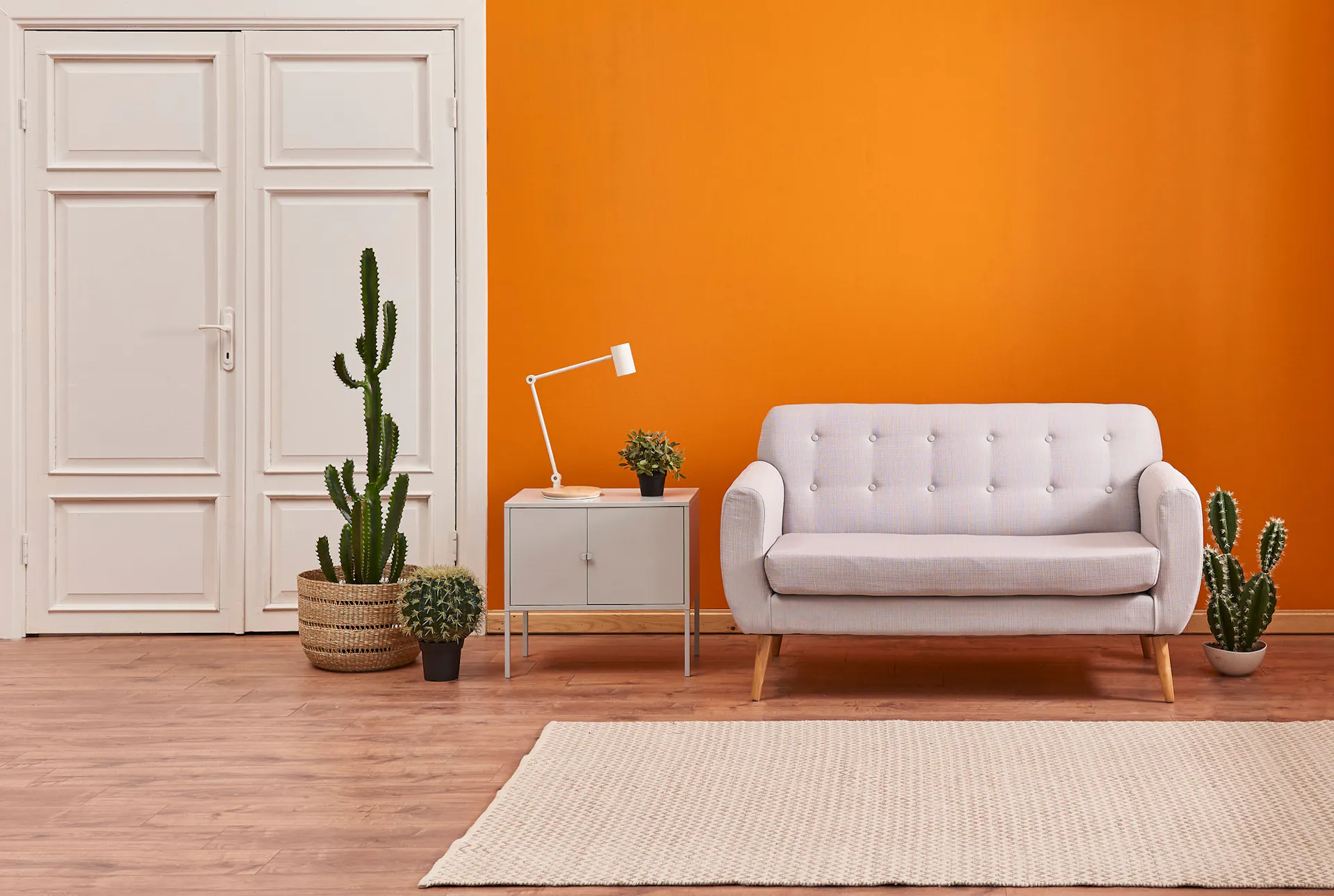 Dans le salon, un canapé est placé devant un mur orange, à côté de cactées et d’une table d'appoint.