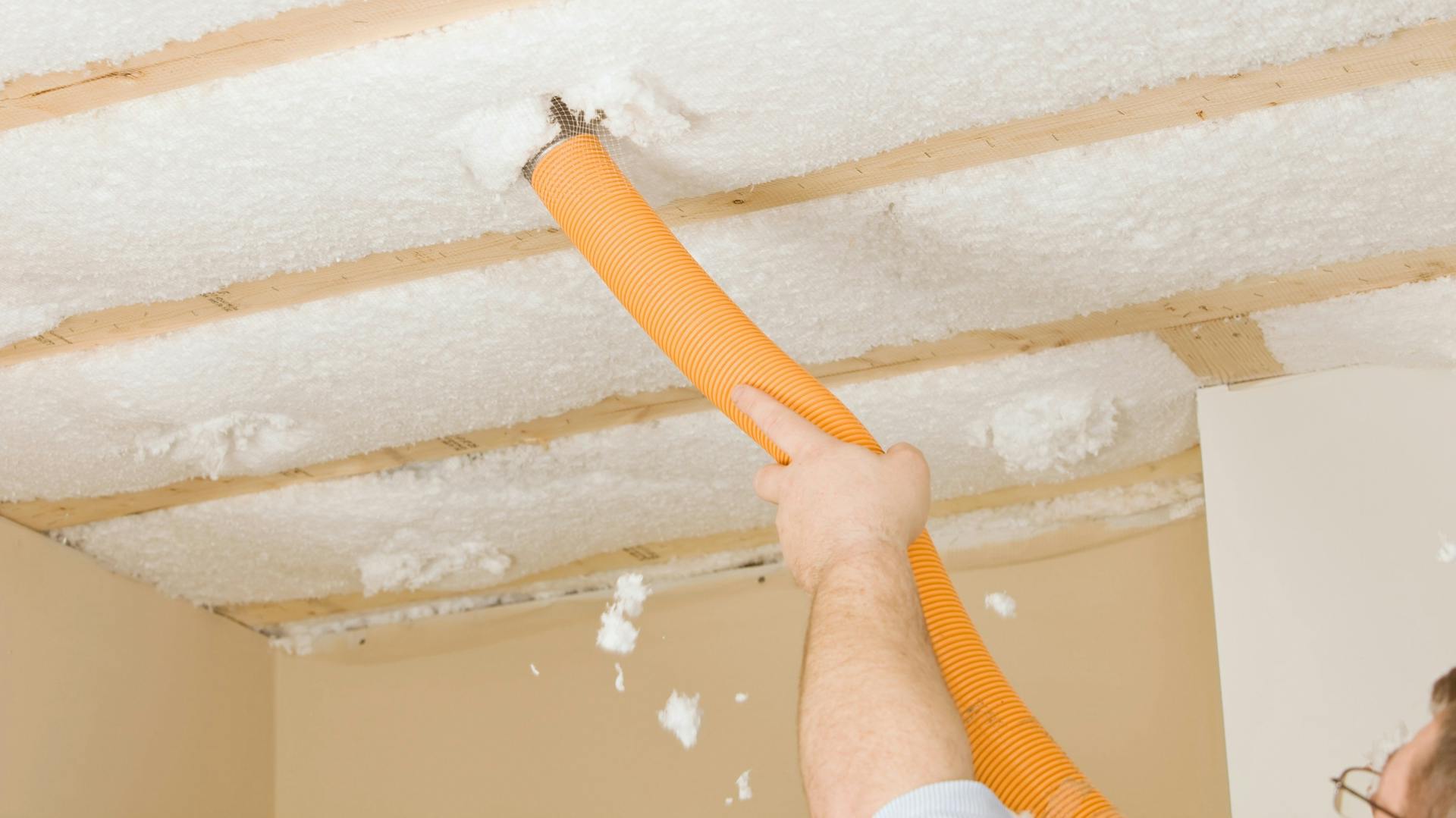 Eine Person bringt die Einblasdämmung an einer Zimmerdecke mithilfe eines Schlauchs ein.