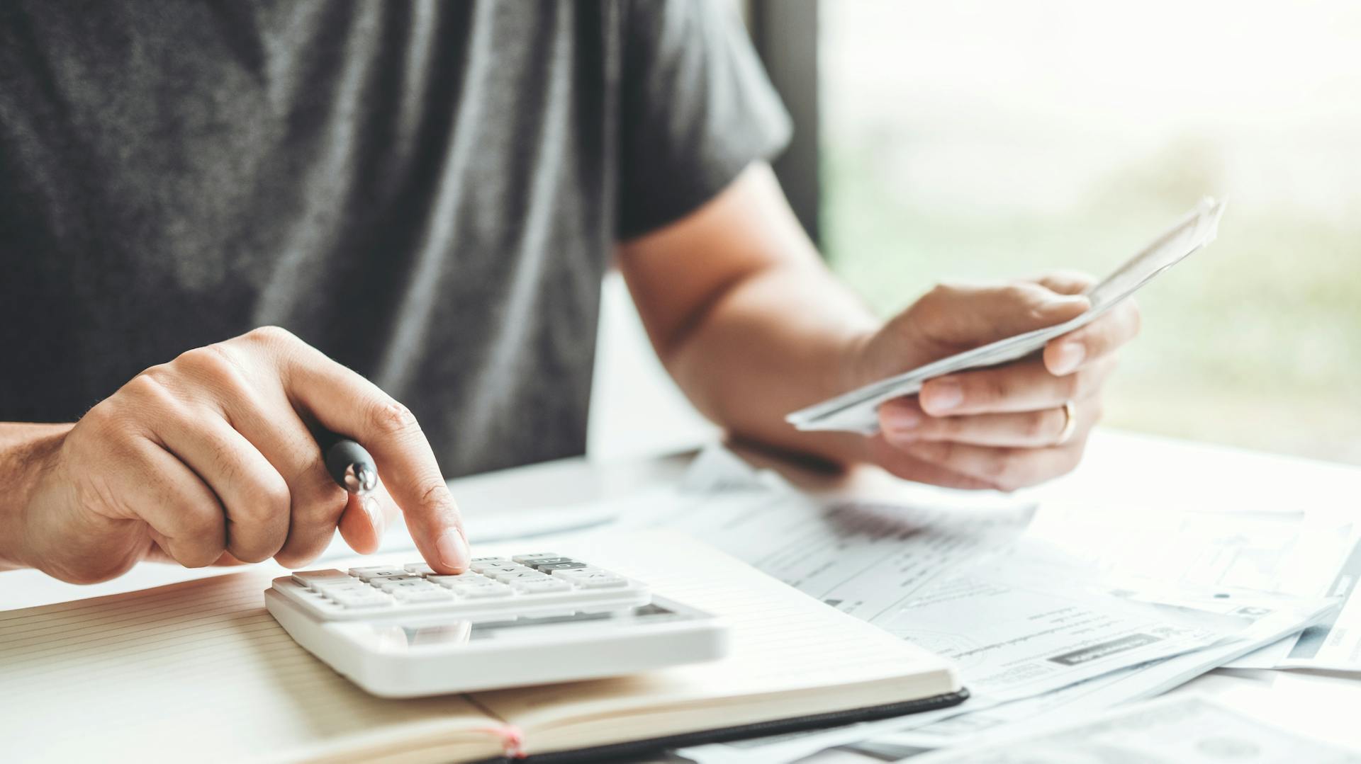 Jemand tippt etwas auf einem Taschenrechner und hält in der anderen Hand Unterlagen.