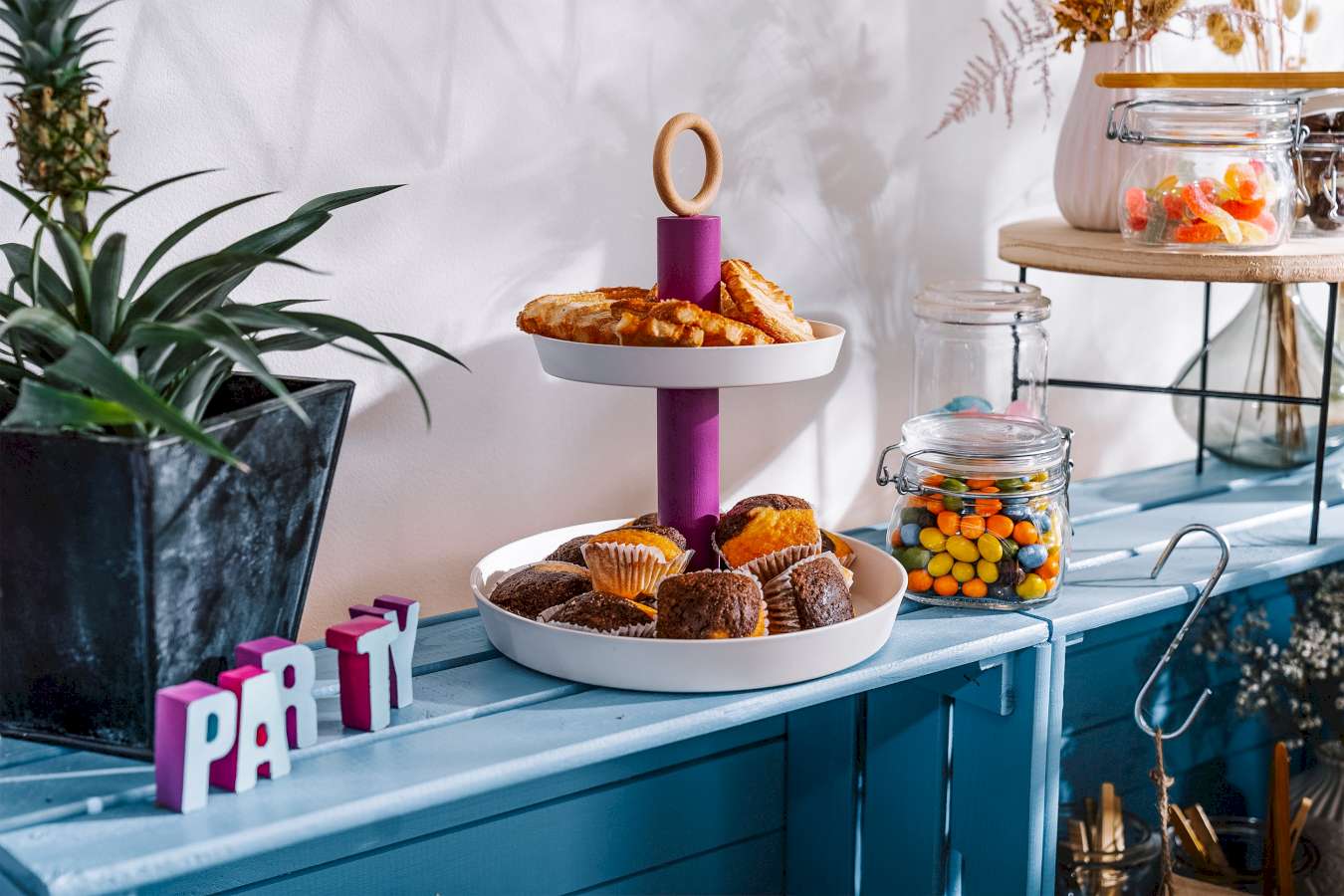 Eine DIY-Etagere, in der sich Gebäck befindet, steht auf einem Regal neben Drahtbügelgläsern mit Süßigkeiten.