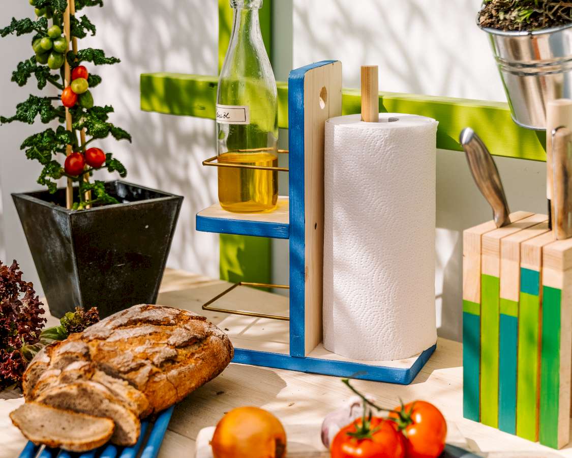 Eine DIY-Küchenrollenhalterung, auf der an einer Seite eine Flasche Öl steht, ist zwischen Lebensmitteln und einem Messerblock platziert..