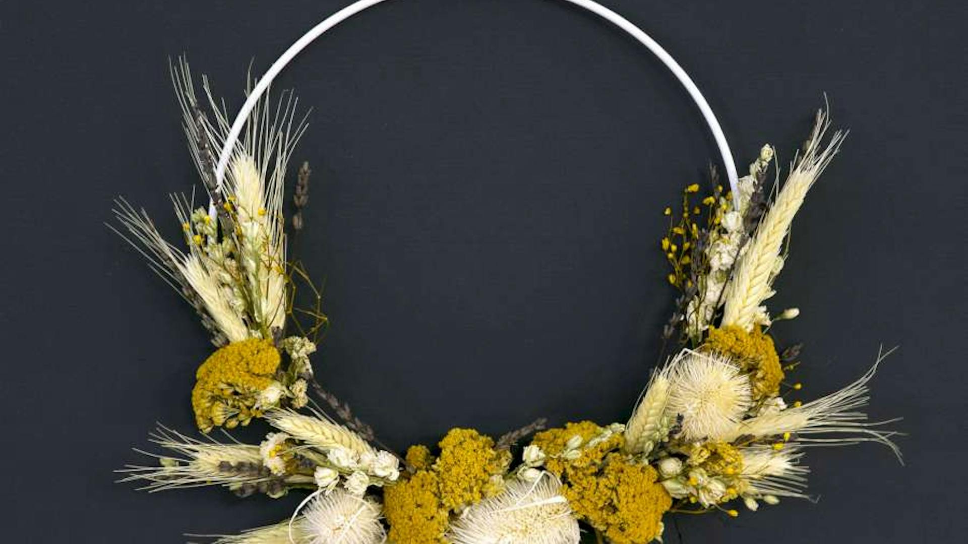 Ein Kranz mit Trockenblumen vor einer dunkelblauen Wand.