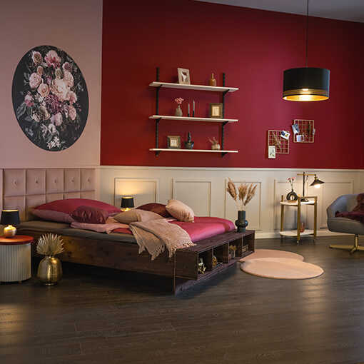 Bett Wilhelm, welches Wandkissen als Bettkopfteil nutzt, steht links in einem bordeaux-roten Raum, der durchzogen wird von einer weißen Kassettierung.