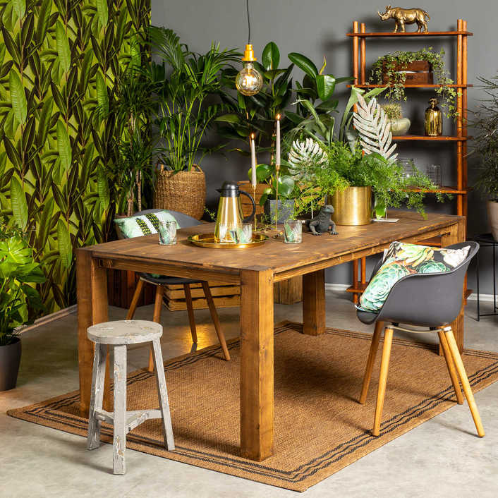 Tisch Maren steht in einem Jungle-Look-Esszimmer mit einer Tapete mit Blattmotiv. Es stehen viele Pflanzen und Tierfiguren auf dem Tisch und um ihn herum. 