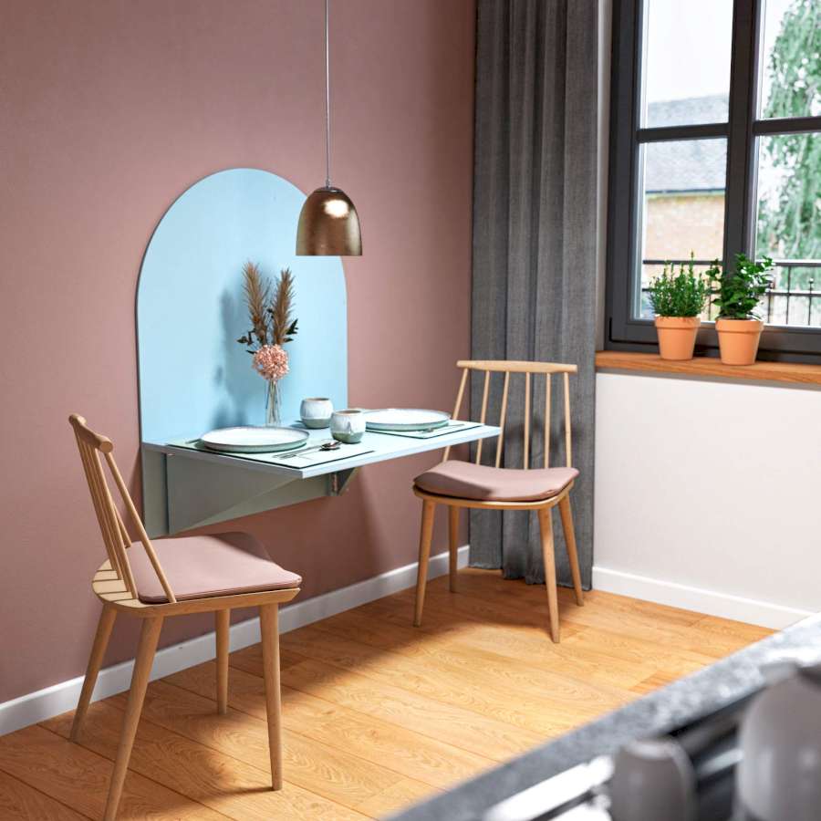 Ein hellblauer DIY-Klapptisch hängt zwischen zwei Stühlen an einer rot-brauen Wand. Auf dem Klapptisch steht Geschirr. 