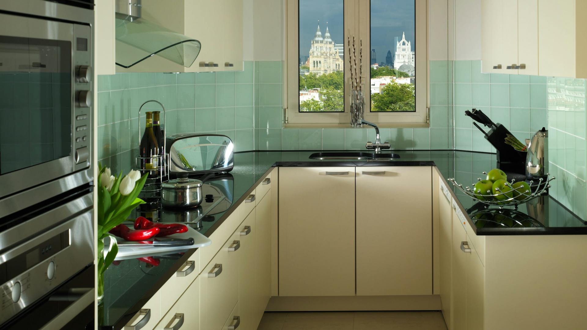 Schmale, helle Küche mit türkisem Fliesenspiegel und schwarzer Arbeitsplatte.