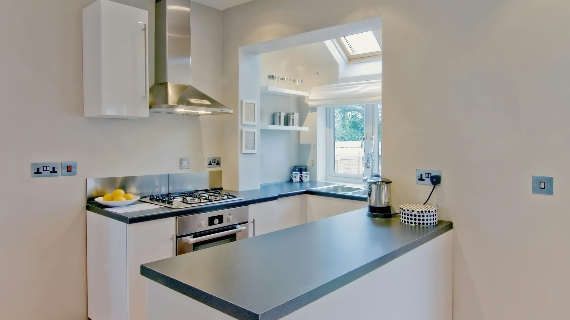 Schmale, moderne Küche mit weißen Schränken und dunkler Arbeitsplatte mit Kücheninsel