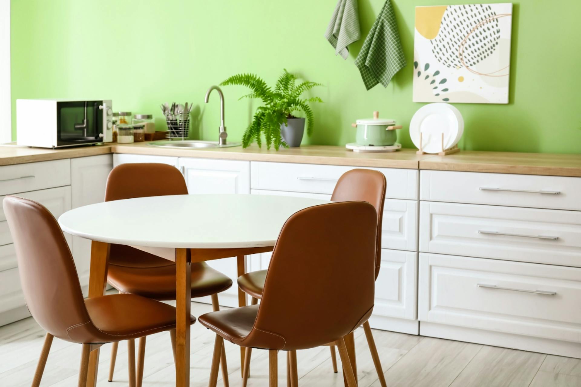 Fehér konyhabútor fa munkalappal zöld fal előtt, étkezőasztal székekkel