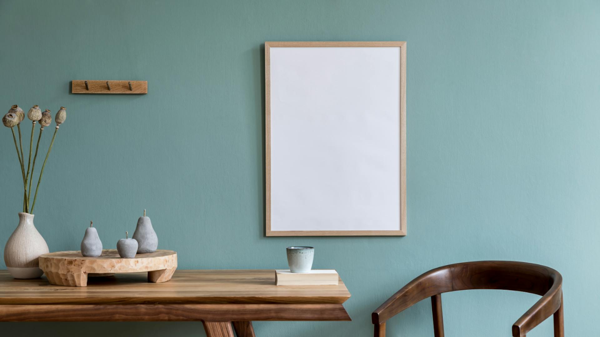 Tavolo di legno con sedia davanti a una parete grigio-blu con un quadro bianco