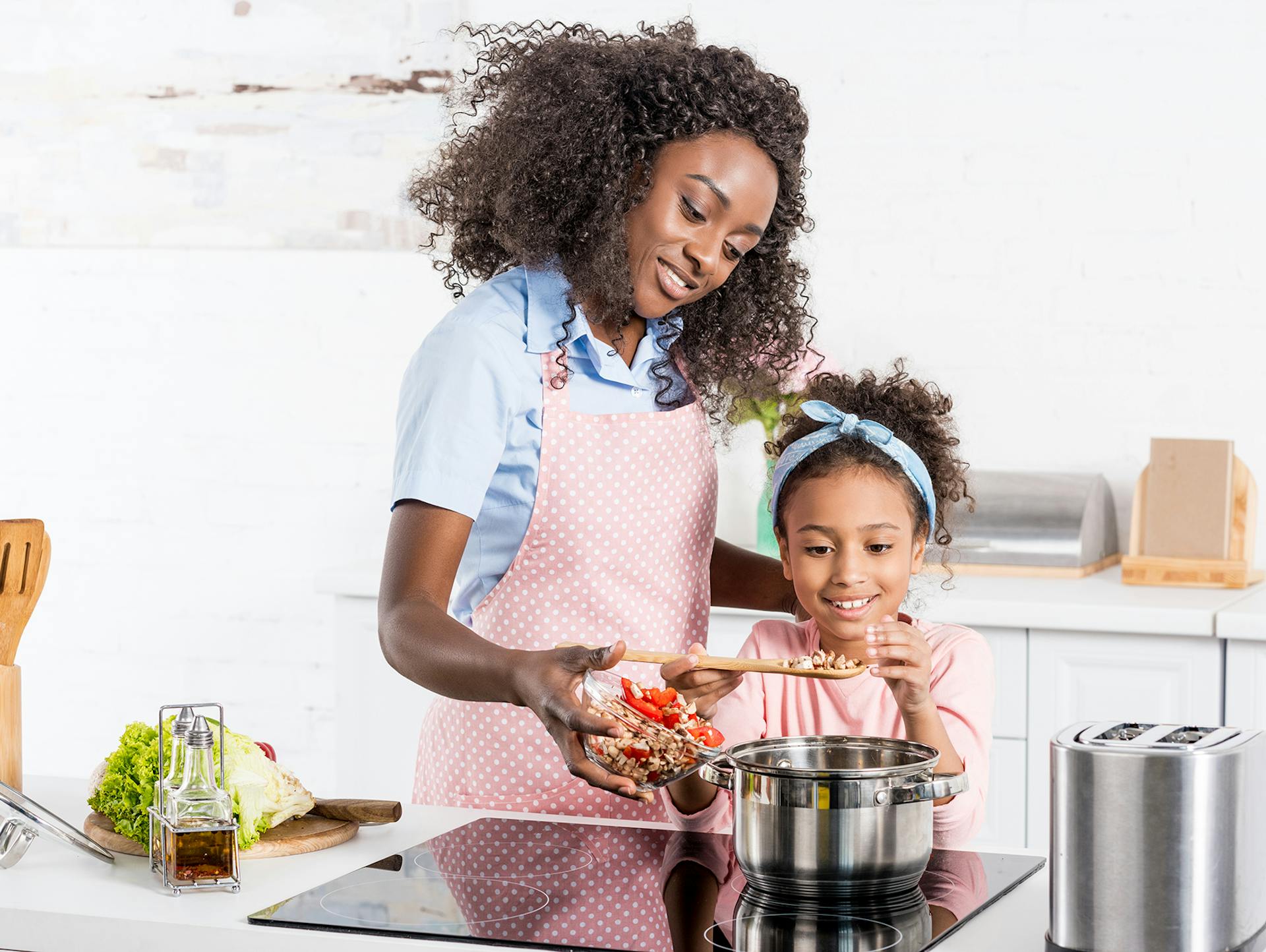 Mutter und Tochter kochen gemeinsam an Herd in Küche.