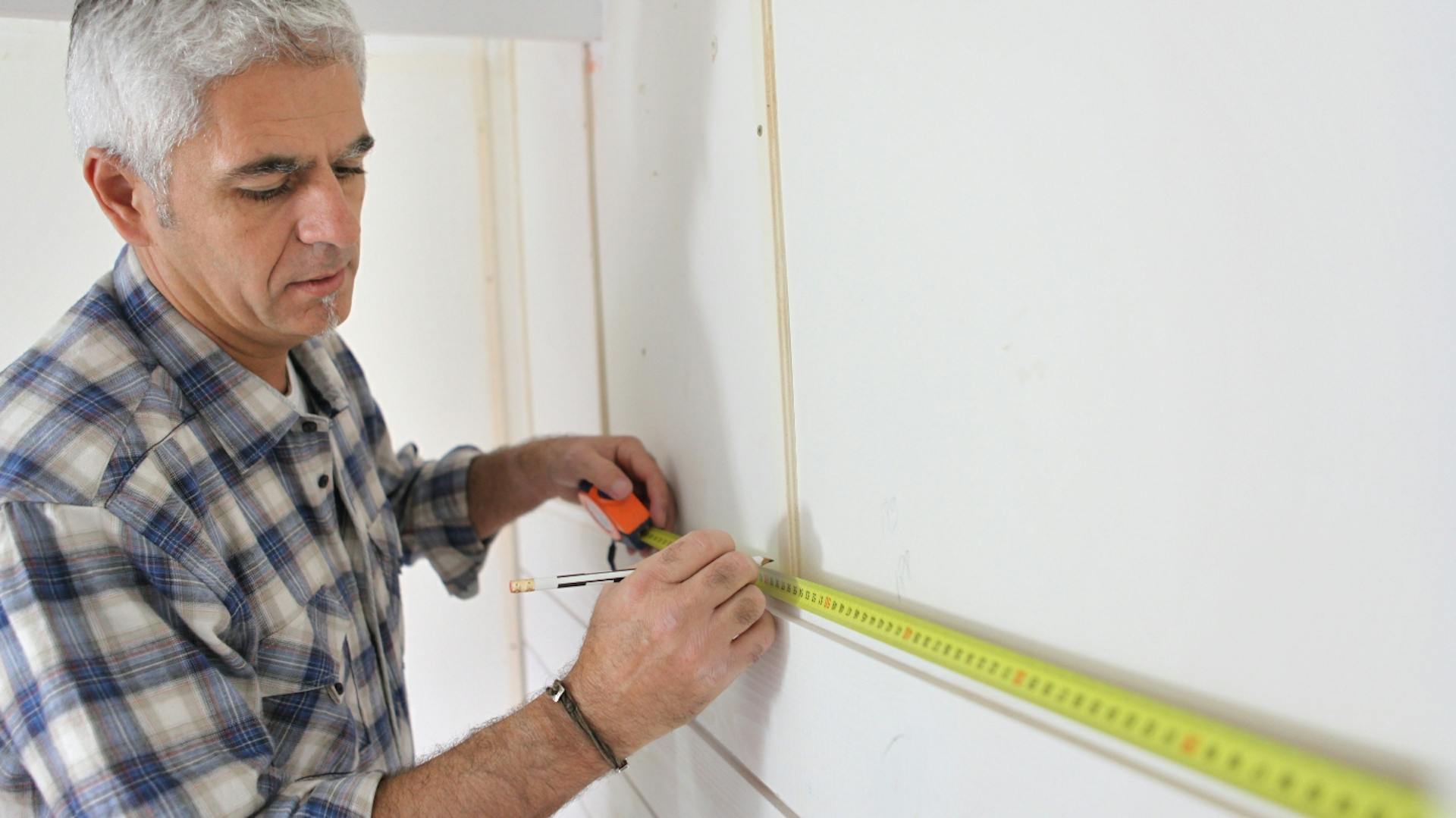 Osoba meria kuchynskú stenu zvinovacím metrom.